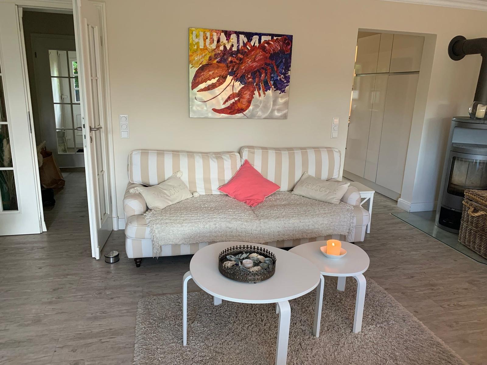 Wohnzimmer mit Sofa, Kissen und Couchtisch. Wandbild zeigt Hummer. Holzfußboden und Teppich.