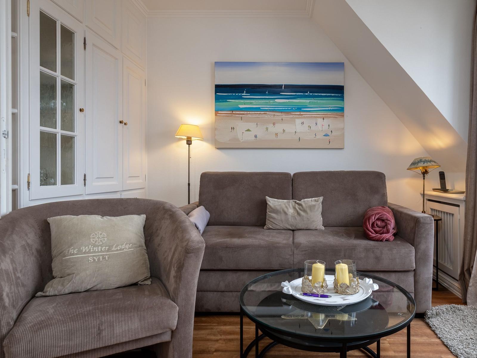 Wohnzimmer mit Sofa, Sessel und Wandbild. Holzboden und schräges Dach.