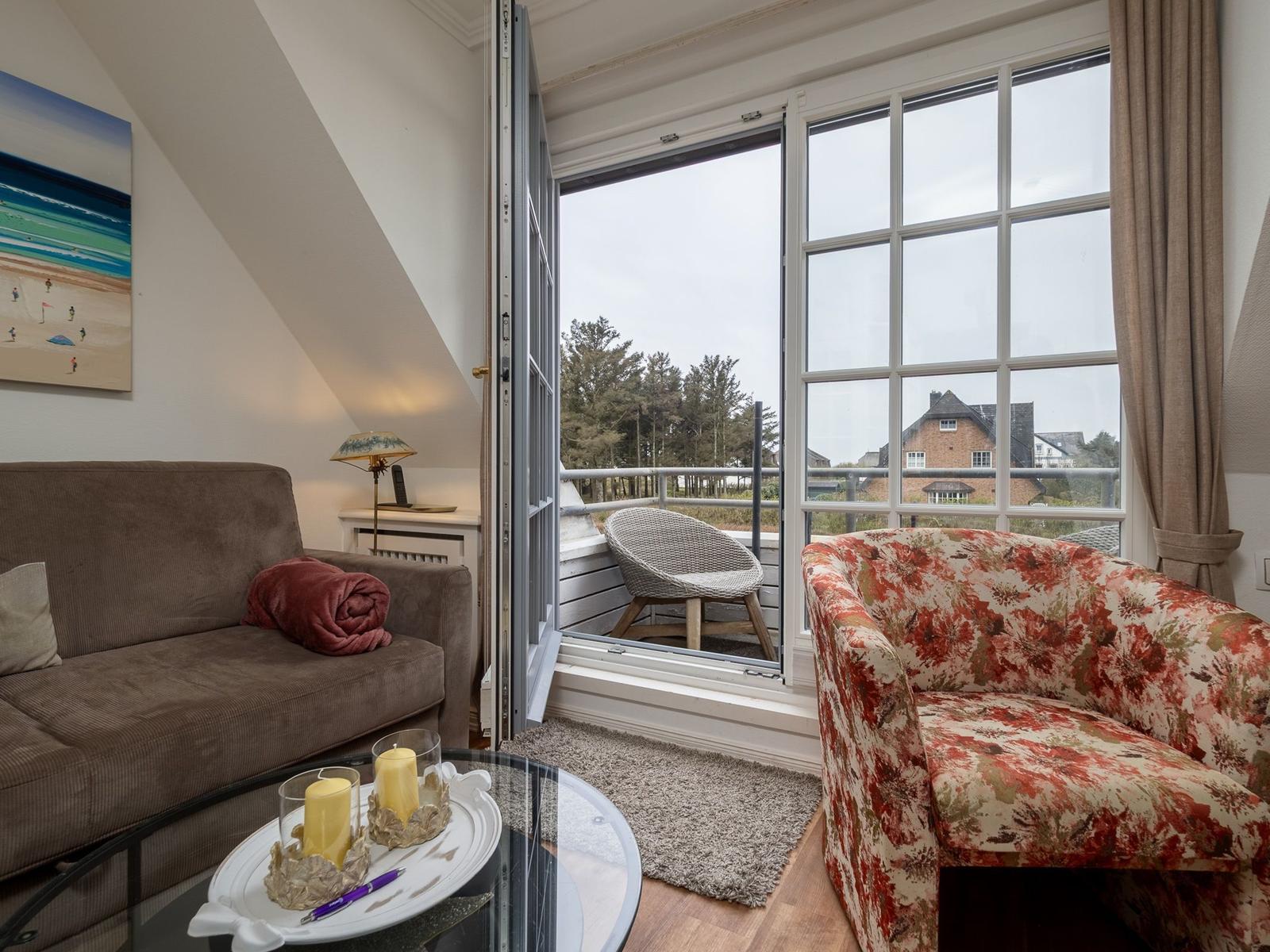 Wohnzimmer mit Sofa, Sessel und Balkon mit Sitzgelegenheit.