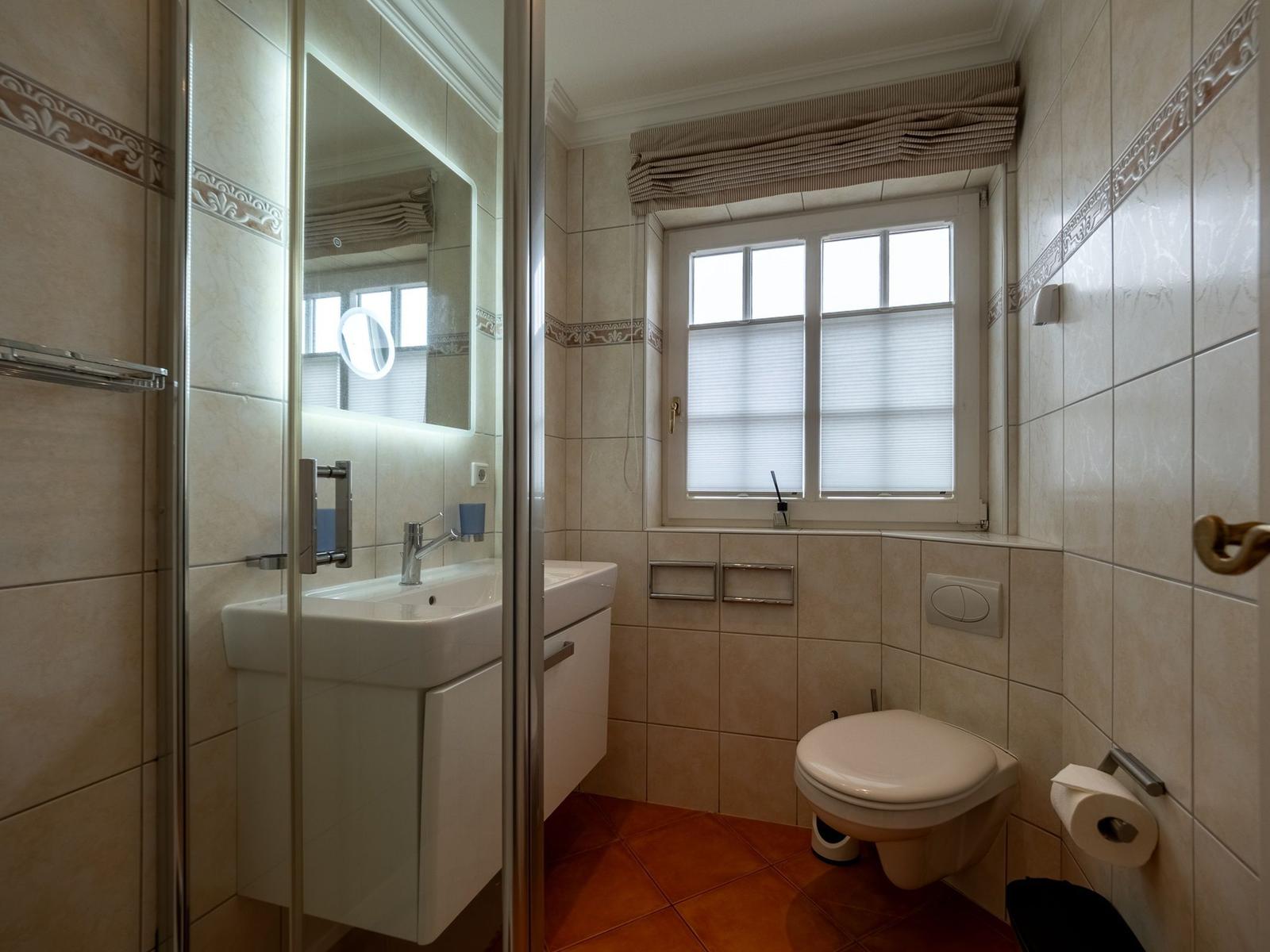 Badezimmer mit Dusche, Waschbecken und Toilette. Fenster mit Jalousie.