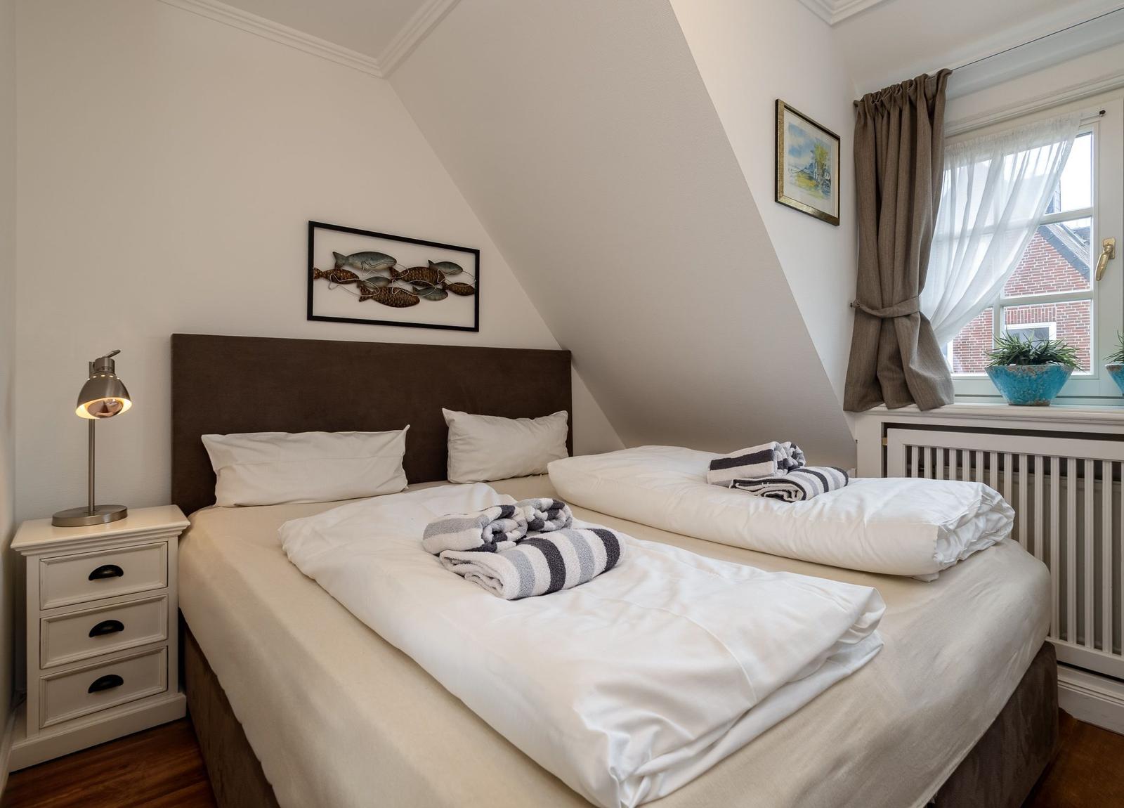 Schlafzimmer mit Doppelbett, Nachttisch und Fenster mit Vorhängen.
