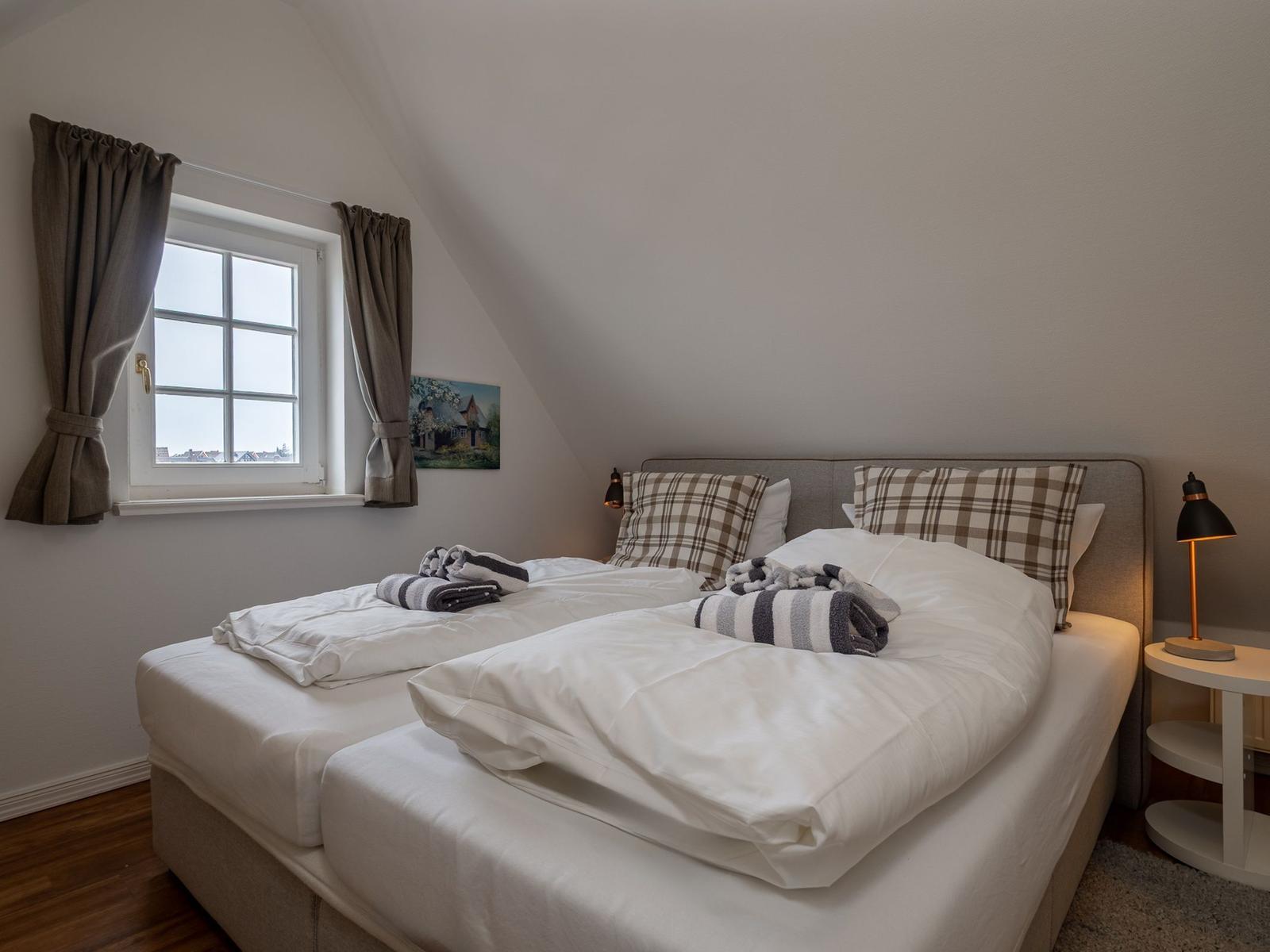 Schlafzimmer mit Doppelbett, Fenster und Nachttisch.