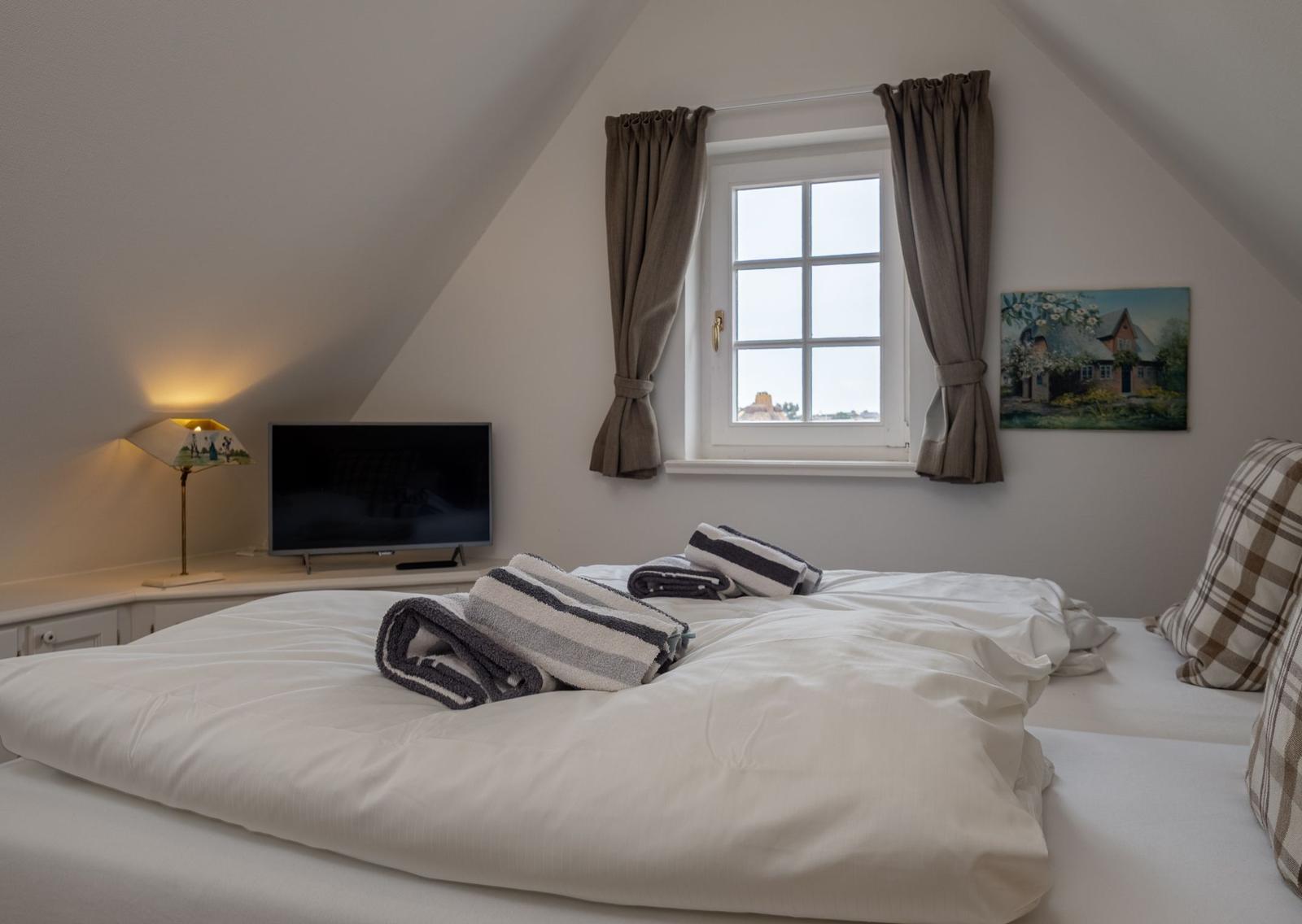 Schlafzimmer mit Dachschrägen, Fenster, Bett und Fernseher.