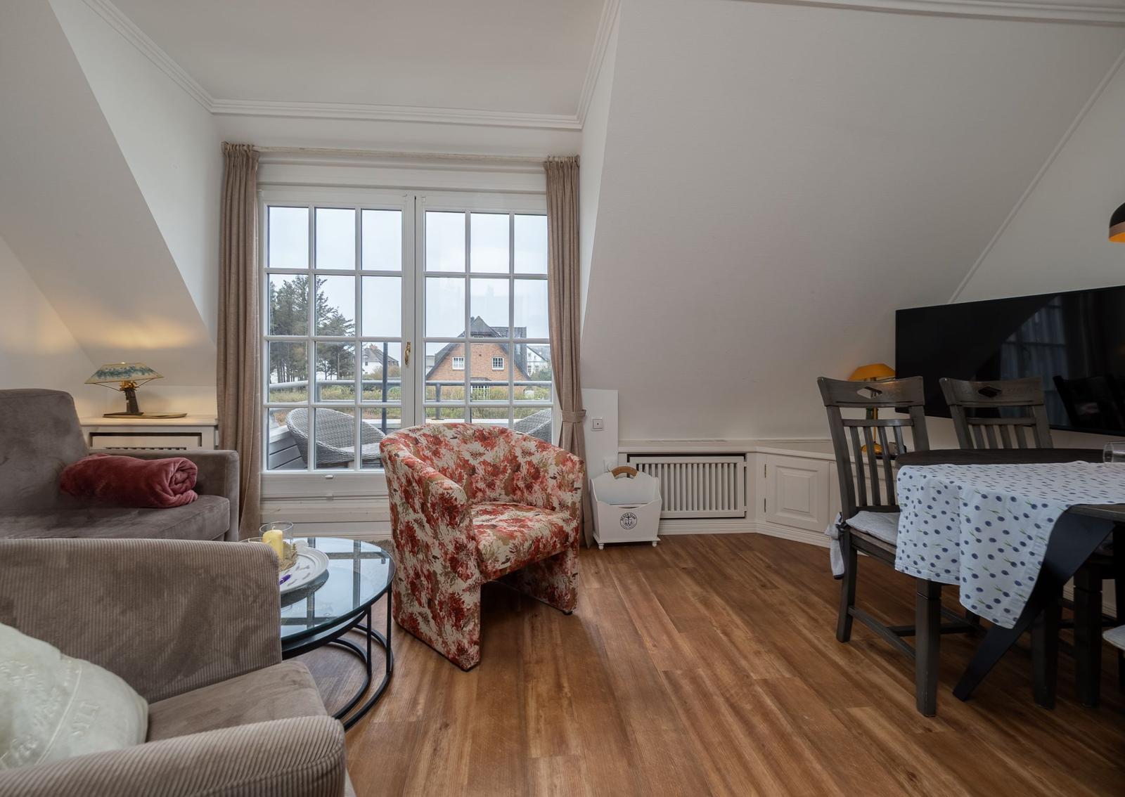 Wohn- und Essbereich mit Holzboden, Fenster und Sitzgelegenheiten.