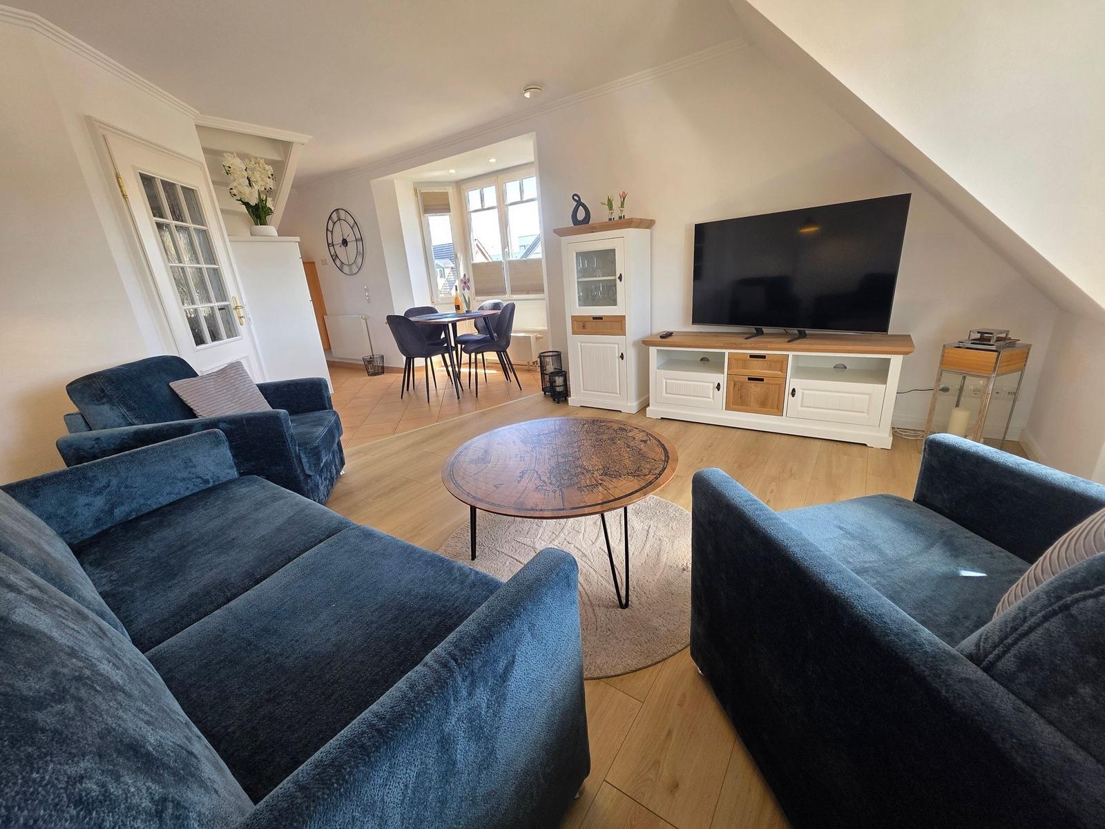 Wohnzimmer mit blauen Sofas, TV und Essbereich im Hintergrund.