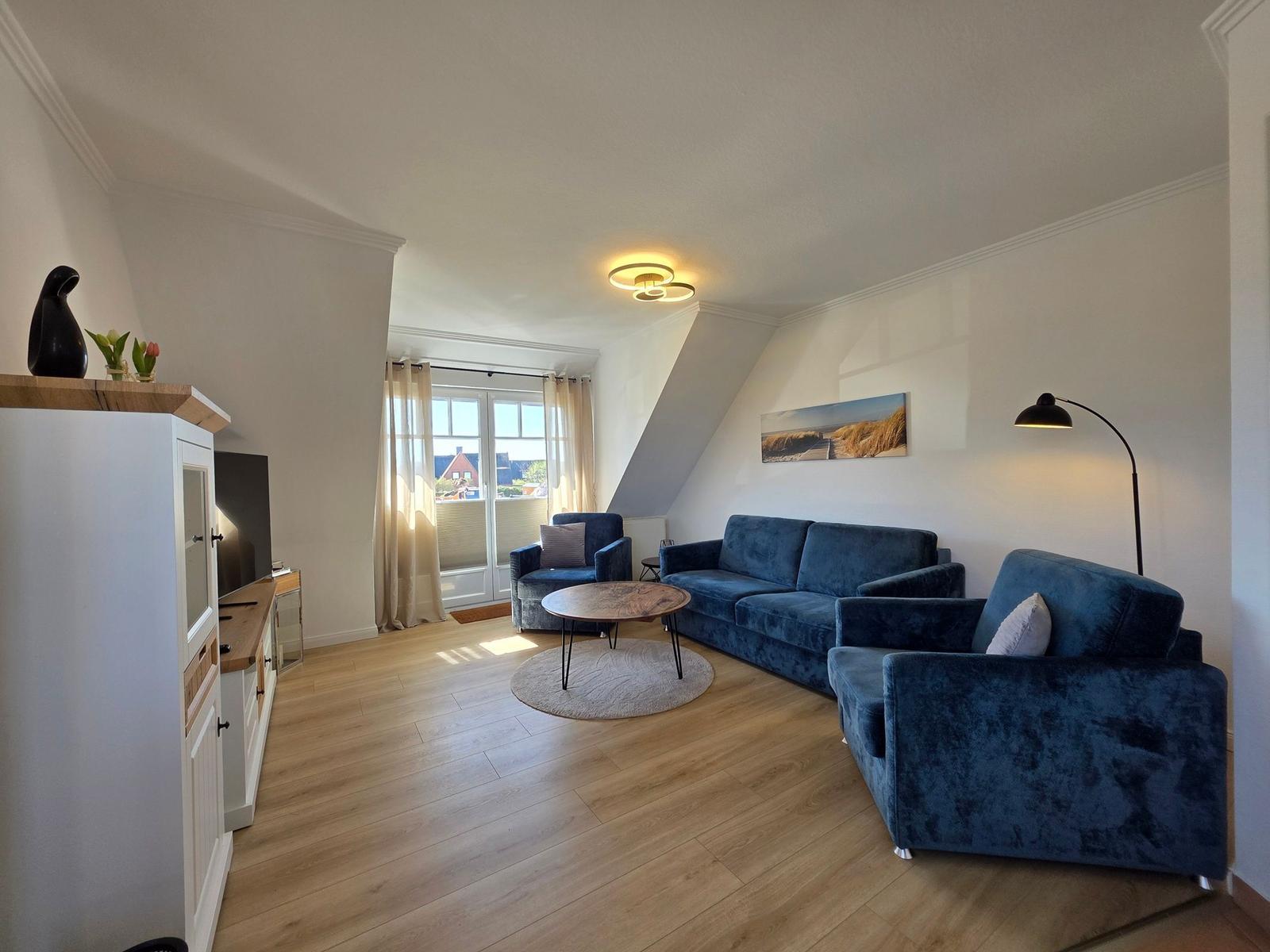 Wohnzimmer mit blauem Sofa, Holzboden und Fenster zur Aussicht.