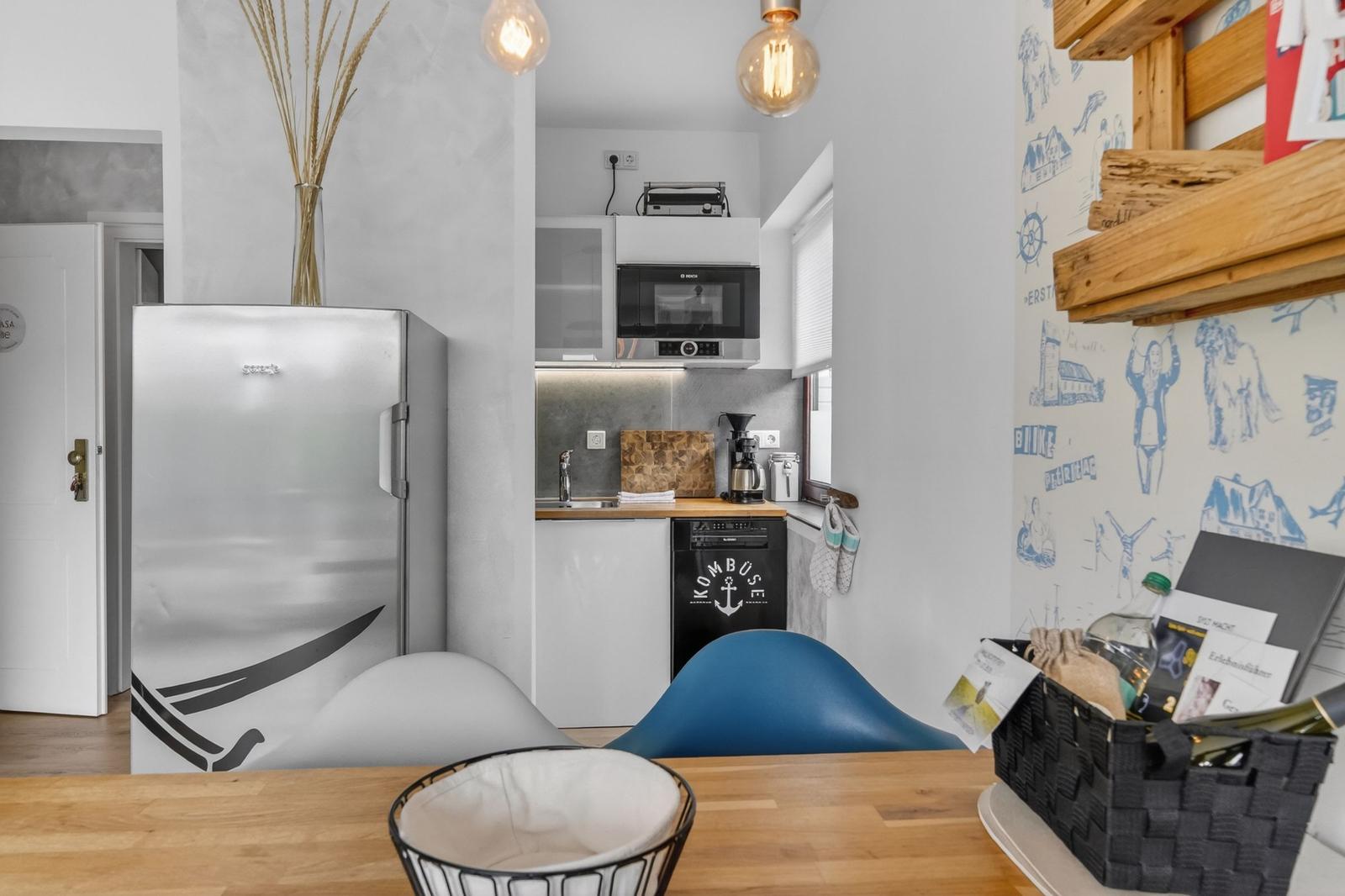 Küche mit Kühlschrank, Mikrowelle und Spülmaschine. Holztisch und blaue Stühle.