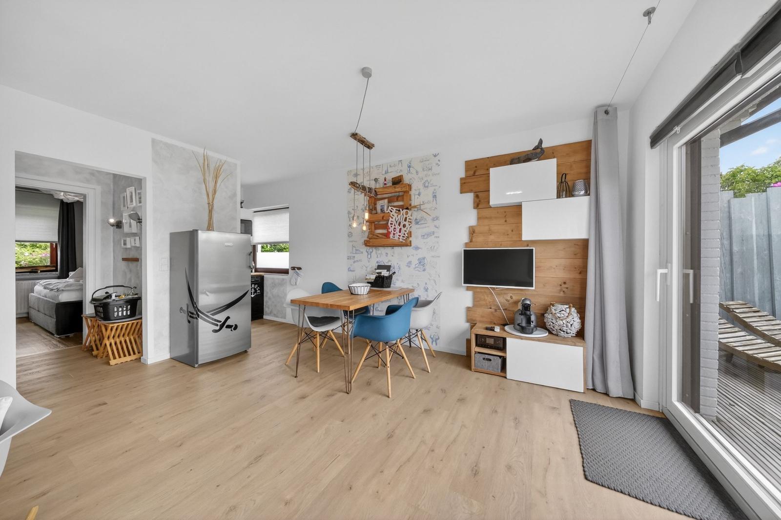 Wohnküche mit Esstisch, Kühlschrank und TV-Wand. Durchgang zur Schlafzimmer.