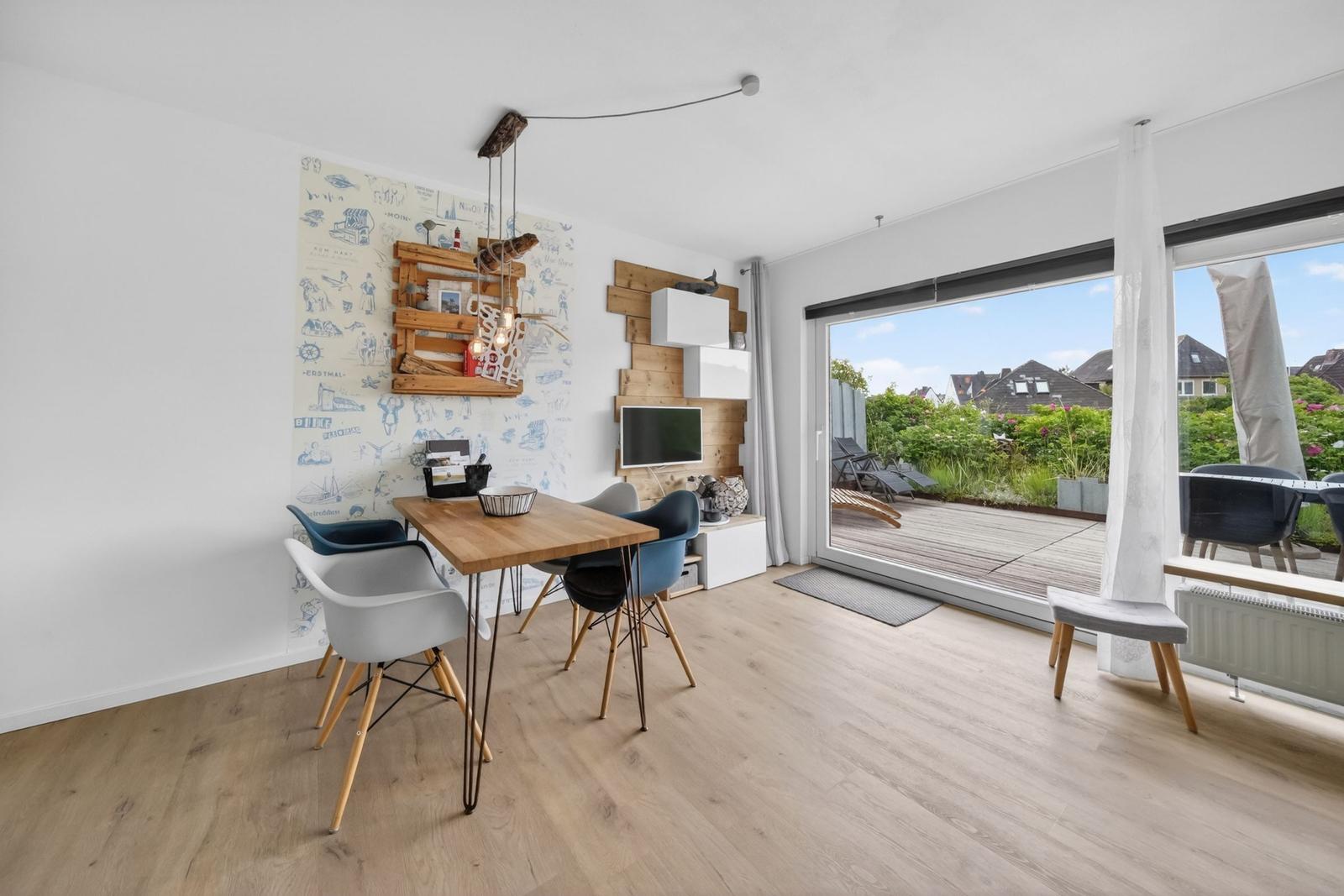 Essbereich mit Tisch und Stühlen, Wand mit Tapete und Holzregal, großes Fenster zur Terrasse.
