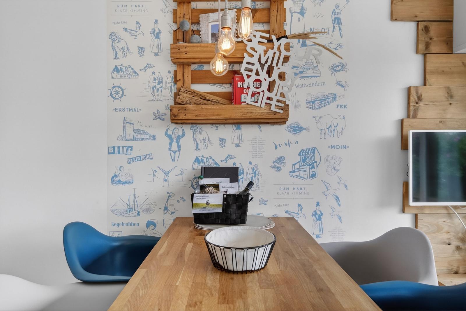 Esstisch mit blauen und grauen Stühlen vor blauem Tapetenwand mit Holzregal.