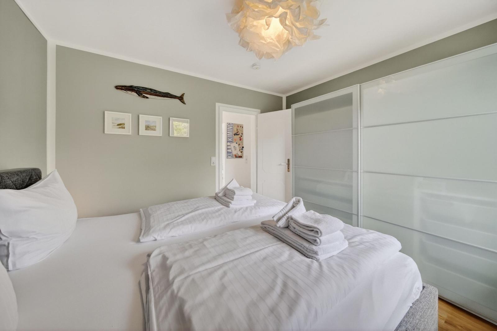 Schlafzimmer mit Doppelbett, weißen Bettwäsche und Glaswand-Schrank.
