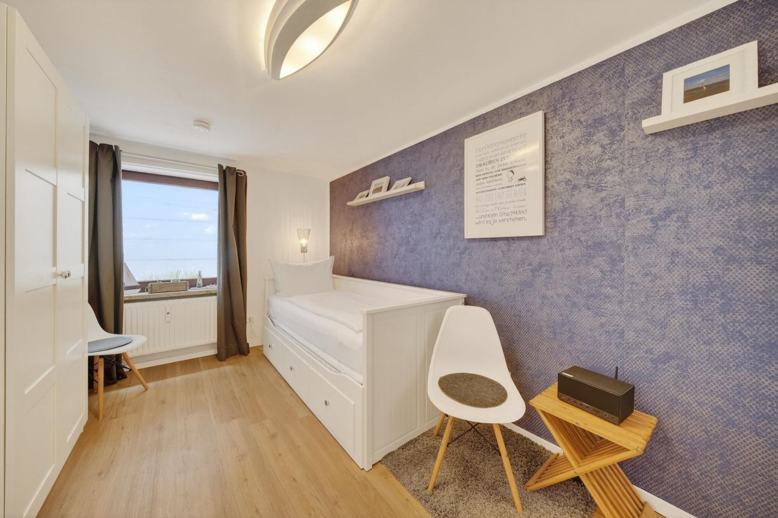 Schlafzimmer mit weißem Bett, lila Wand und Holzboden. Fenster mit Blick auf Wasser.