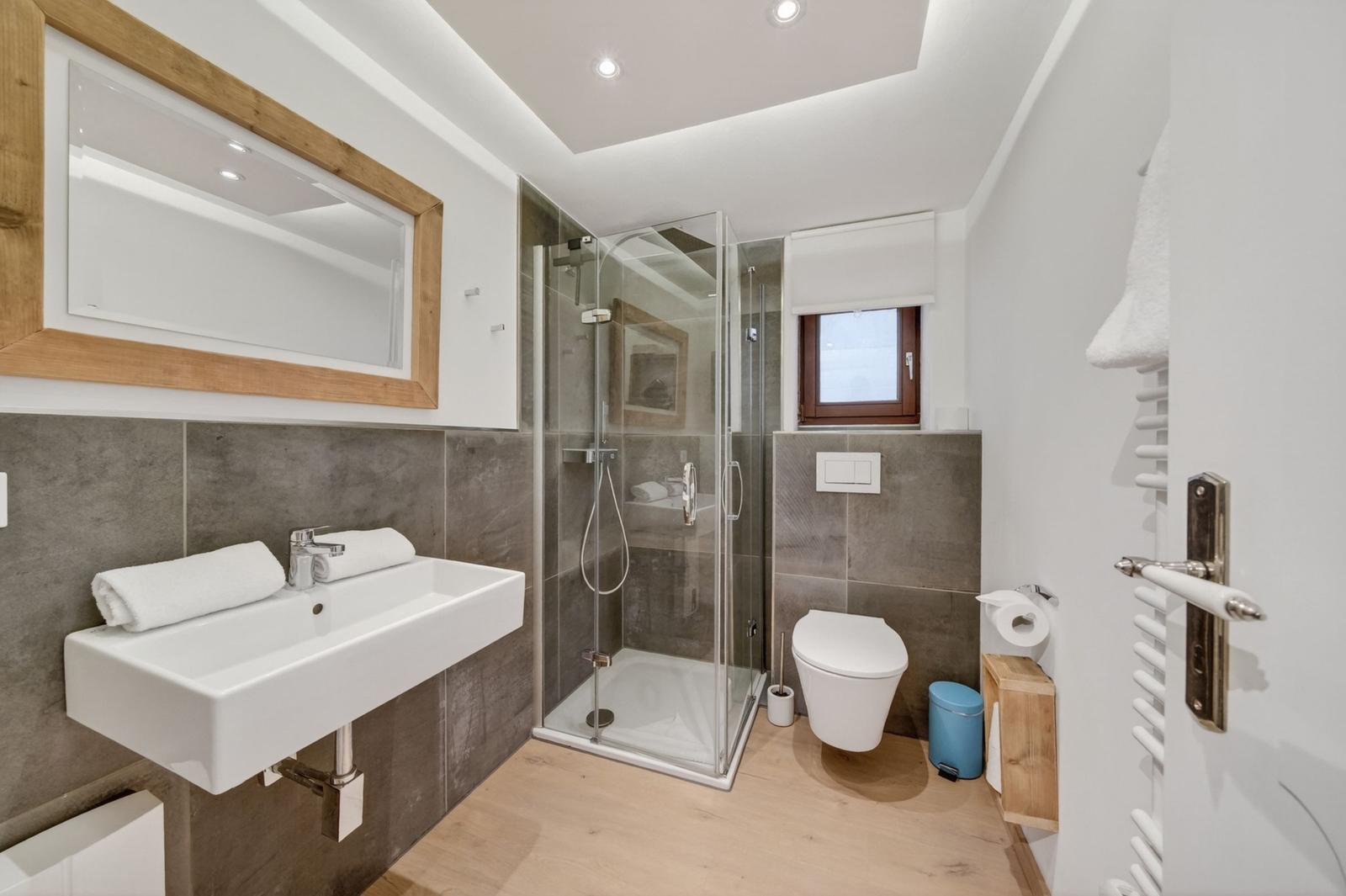 Badezimmer mit Dusche, Waschbecken und Toilette. Holz- und Steinoptik.