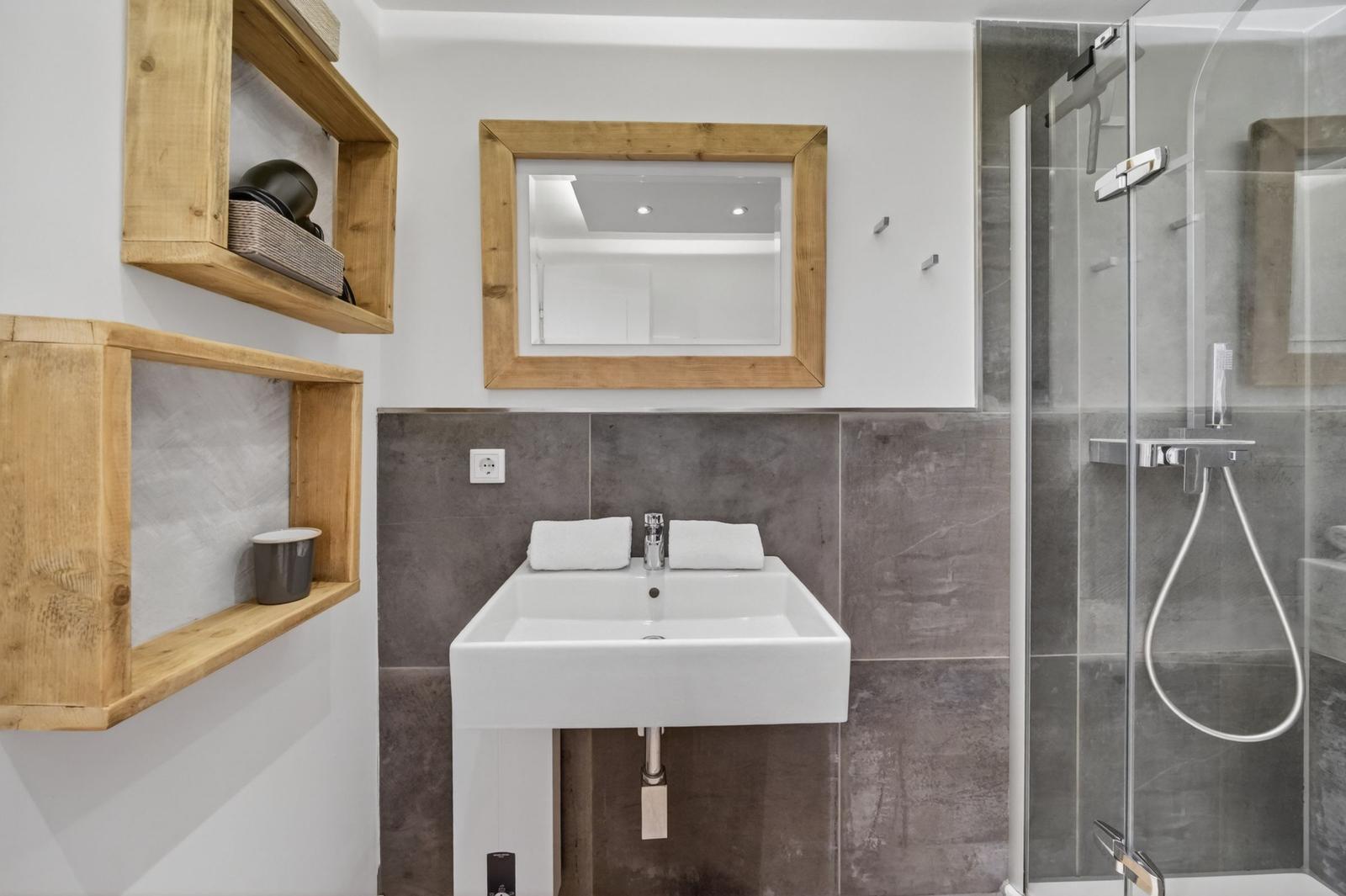 Badezimmer mit Dusche, Waschbecken und Holzregalen an der Wand.