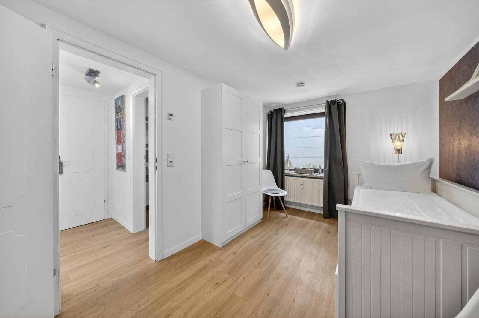 Schlafzimmer mit weißem Bett, Holzboden und Fenster mit Vorhängen.