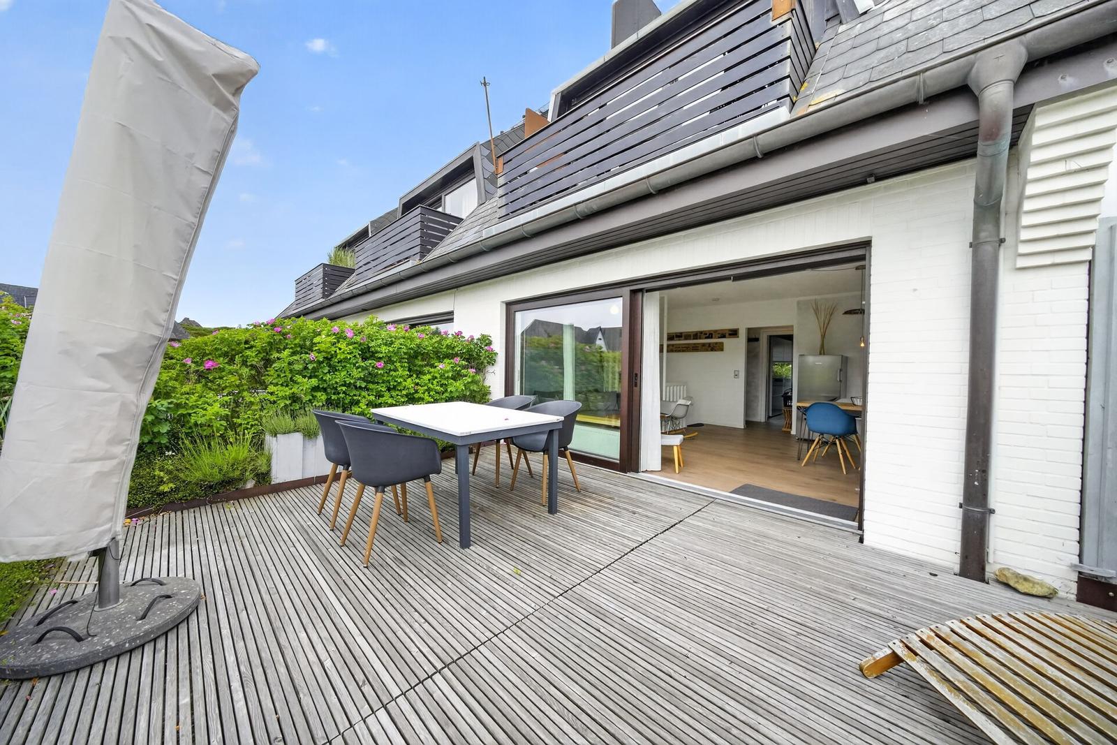 Terrasse mit Tisch, Stühlen und Grillplatz. Durchgang ins Wohnhaus mit Küche.