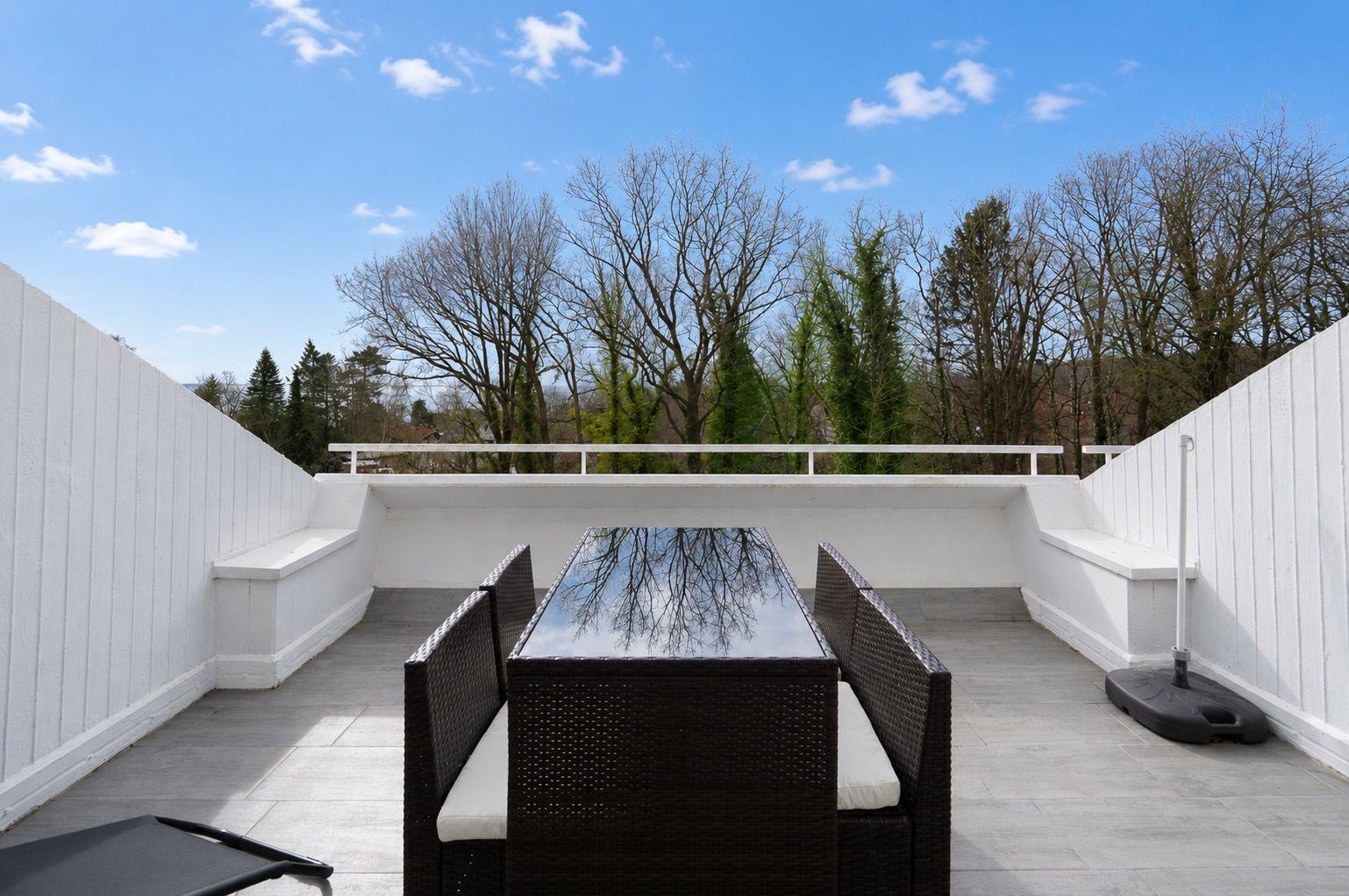 Terrace with table and chairs, view of trees and blue sky.