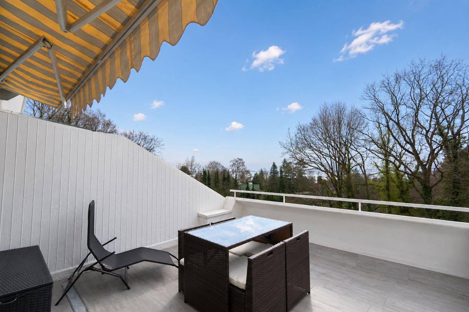 Terrace with table, chairs, and awning. View of trees and sky.