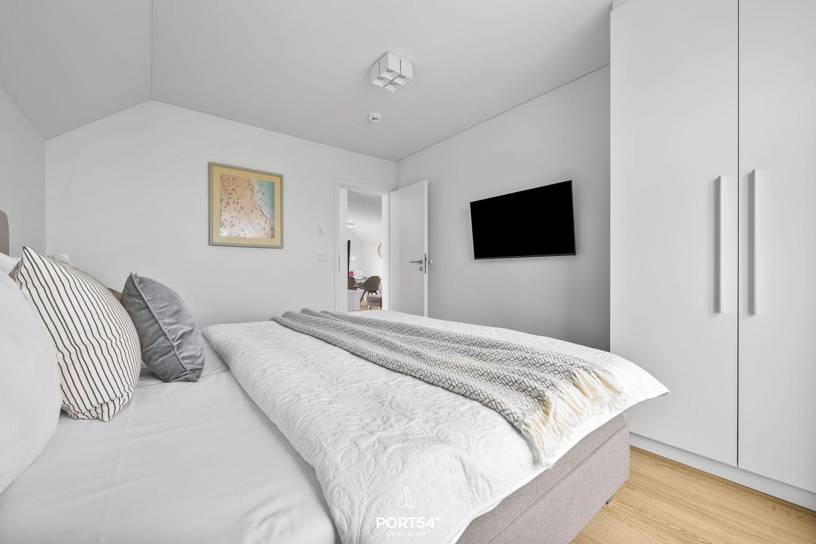 Schlafzimmer mit Bett, TV und Kleiderschrank. Tür führt in Wohnbereich.