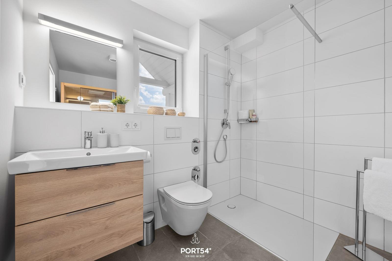 Badezimmer mit Dusche, Waschbecken und Toilette. Fenster mit Blick nach draußen.