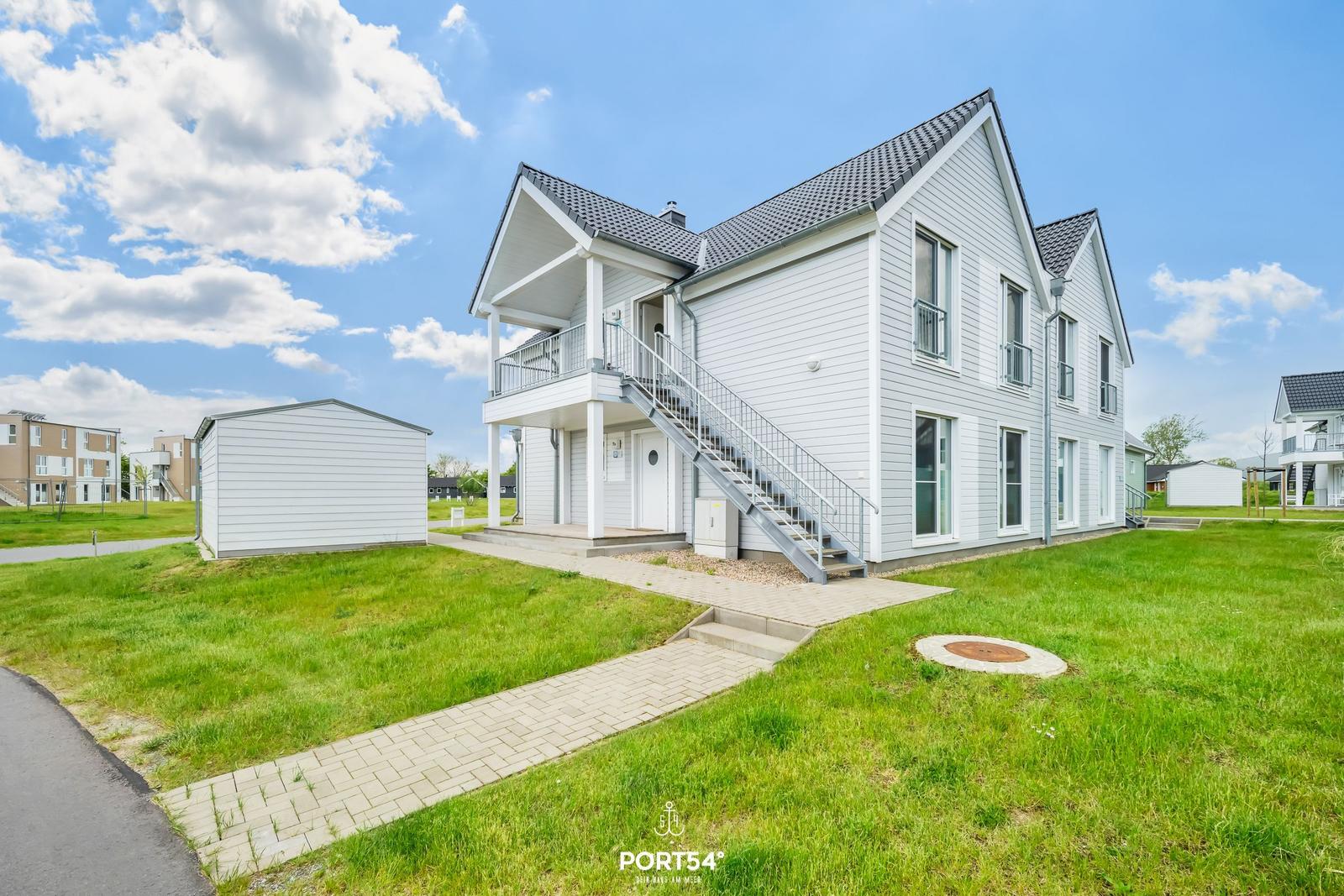 Moderne zweistöckige Villa mit Balkon und Außentreppe auf grünem Grundstück.