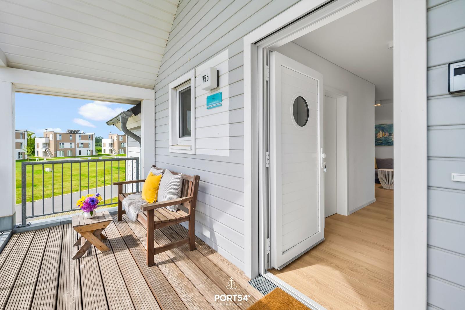 Haus mit Terrasse, Holzbank und Blick auf Grünflächen. Tür führt ins Innere.
