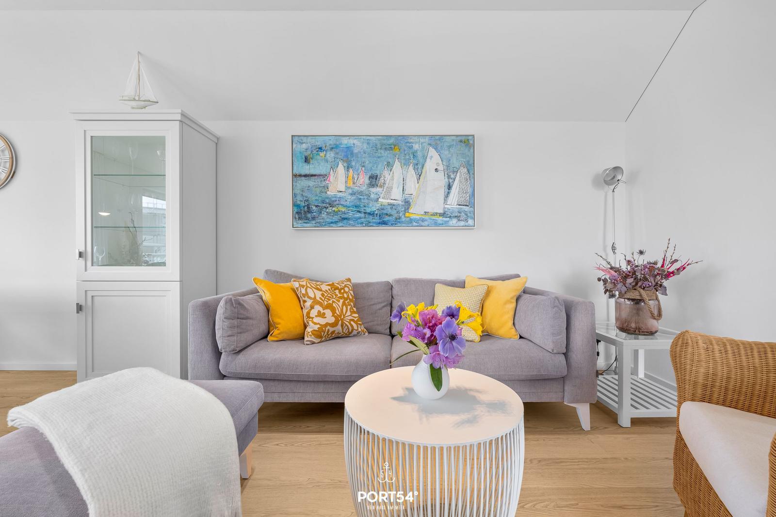 Ein Wohnzimmer mit grauem Sofa, gelben Kissen und einem runden Tisch.