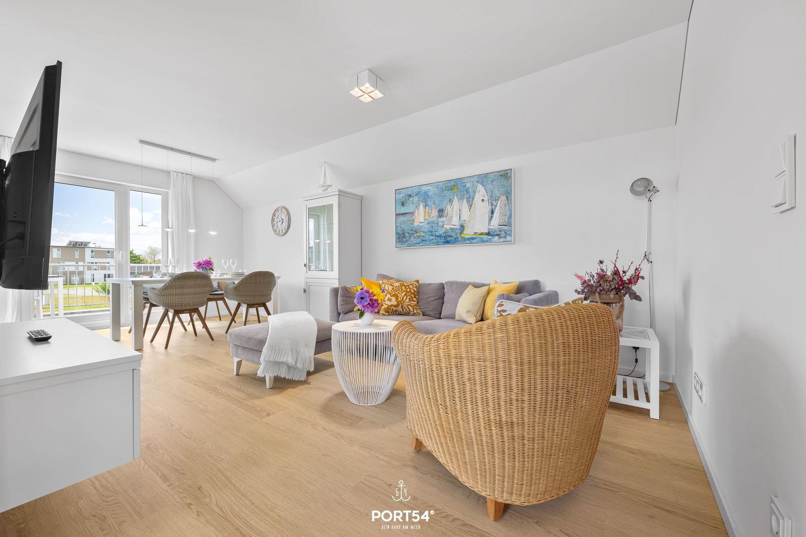 Wohn- und Essbereich mit Sofa, Esstisch und TV. Holzboden und große Fenster.