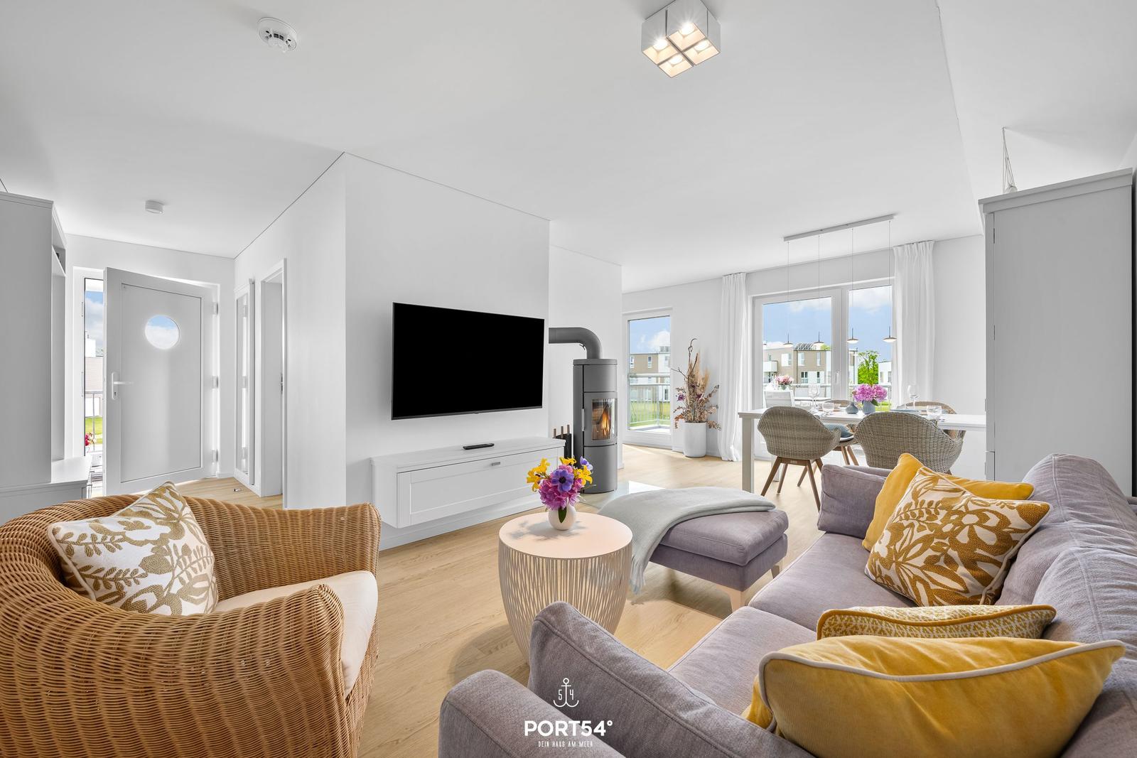 Wohn- und Essbereich mit Sofa, Sessel und Fernseher. Holzboden und große Fenster.