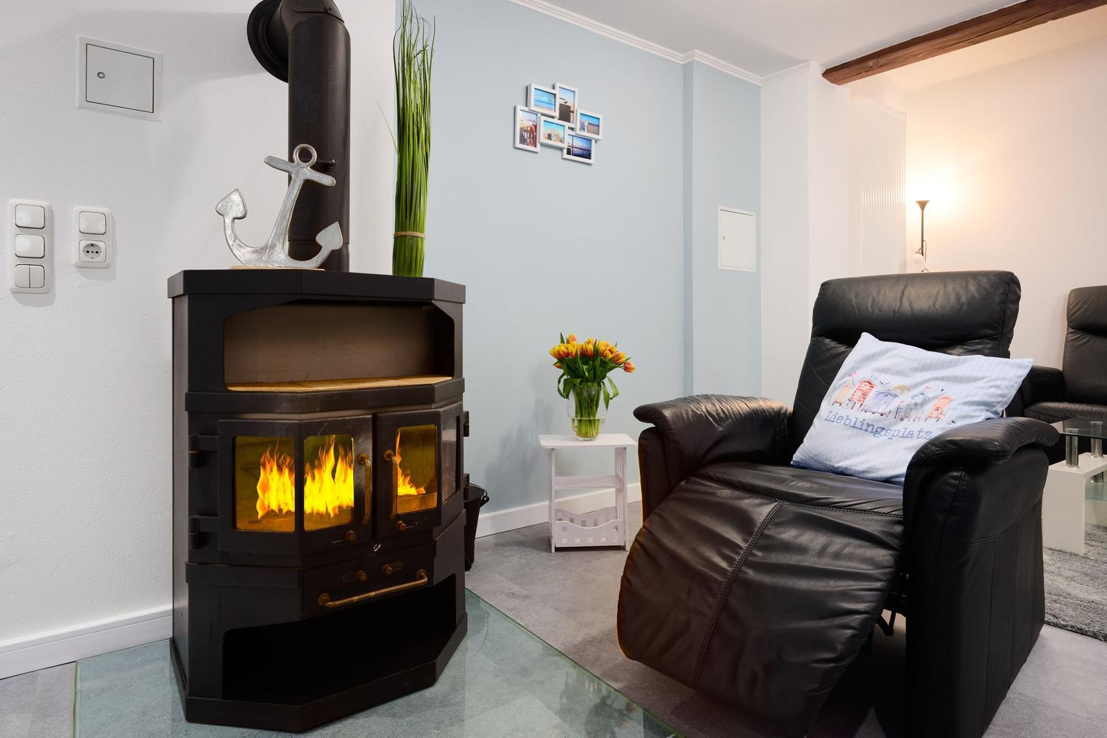 Ein Wohnzimmer mit einem Kaminofen, einem schwarzen Sessel und einer Vase mit Tulpen.
