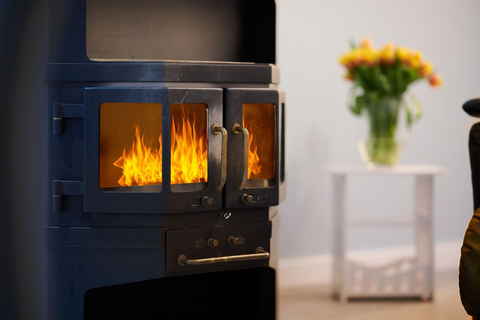 Ein Kaminofen mit brennendem Feuer, daneben ein Tisch mit Blumen.