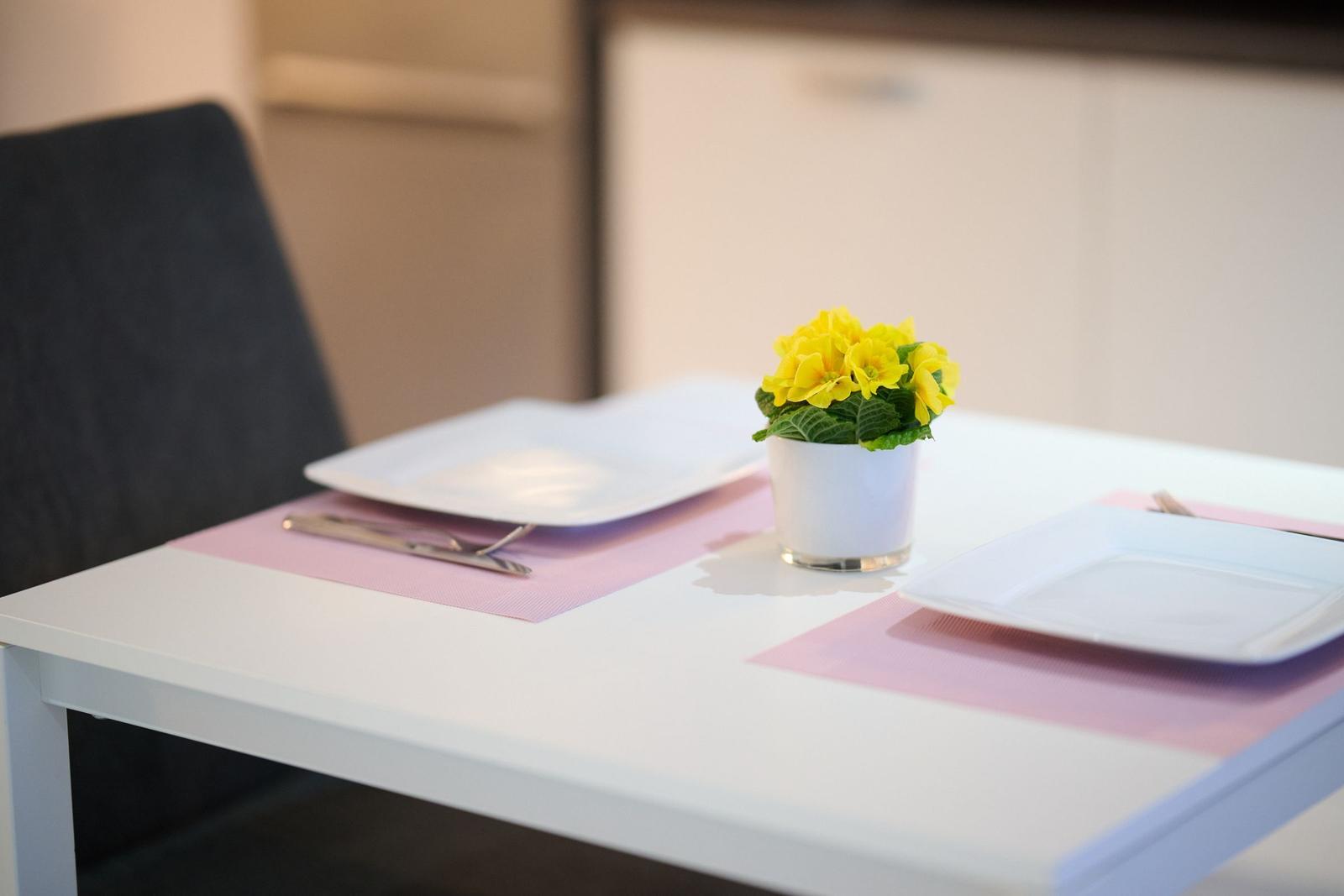 Tisch mit zwei Platzsetzungen und einer Blumenvase in der Mitte.