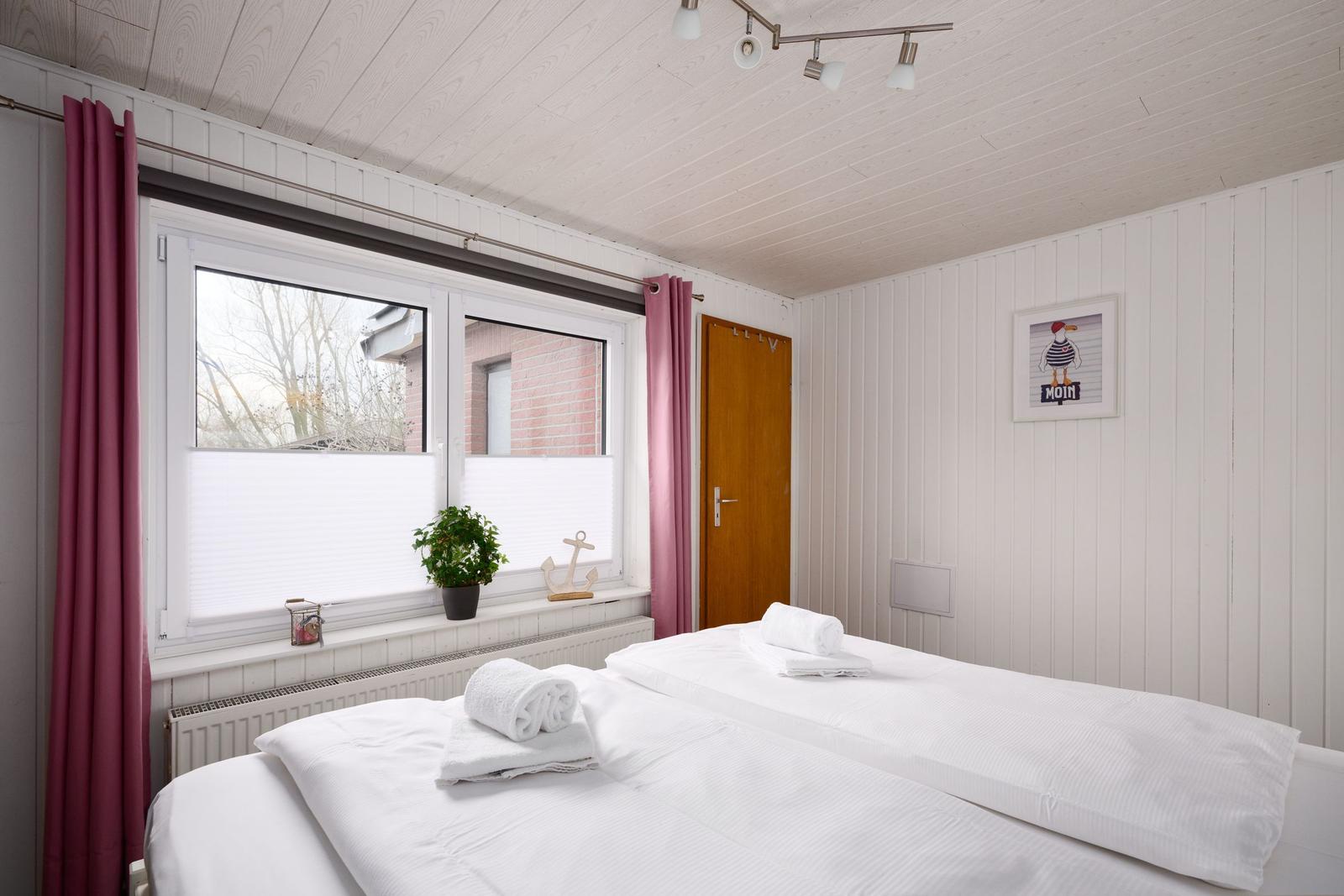 Schlafzimmer mit Doppelbett, Fenster und rosa Vorhängen.