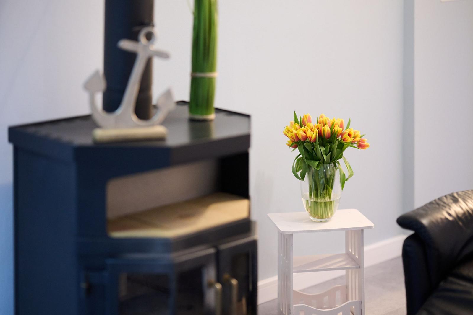 Ein blauer Kamin mit Anker und Bambus. Gelbe Tulpen in einem Glas auf einem weißen Tisch.