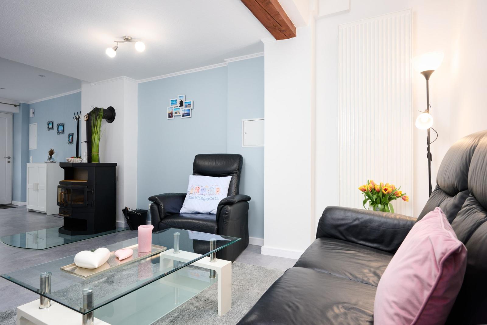 Wohnzimmer mit Sofa, Sessel, Glas-Tisch und Kaminofen.