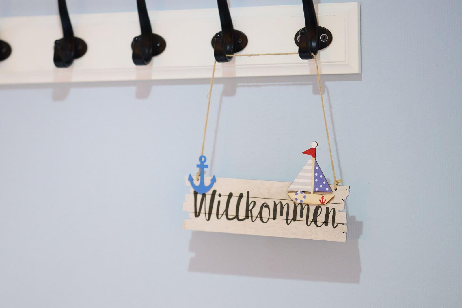 Willkommen-Schild mit Segelboot und Anker hängt an einer Garderobe.