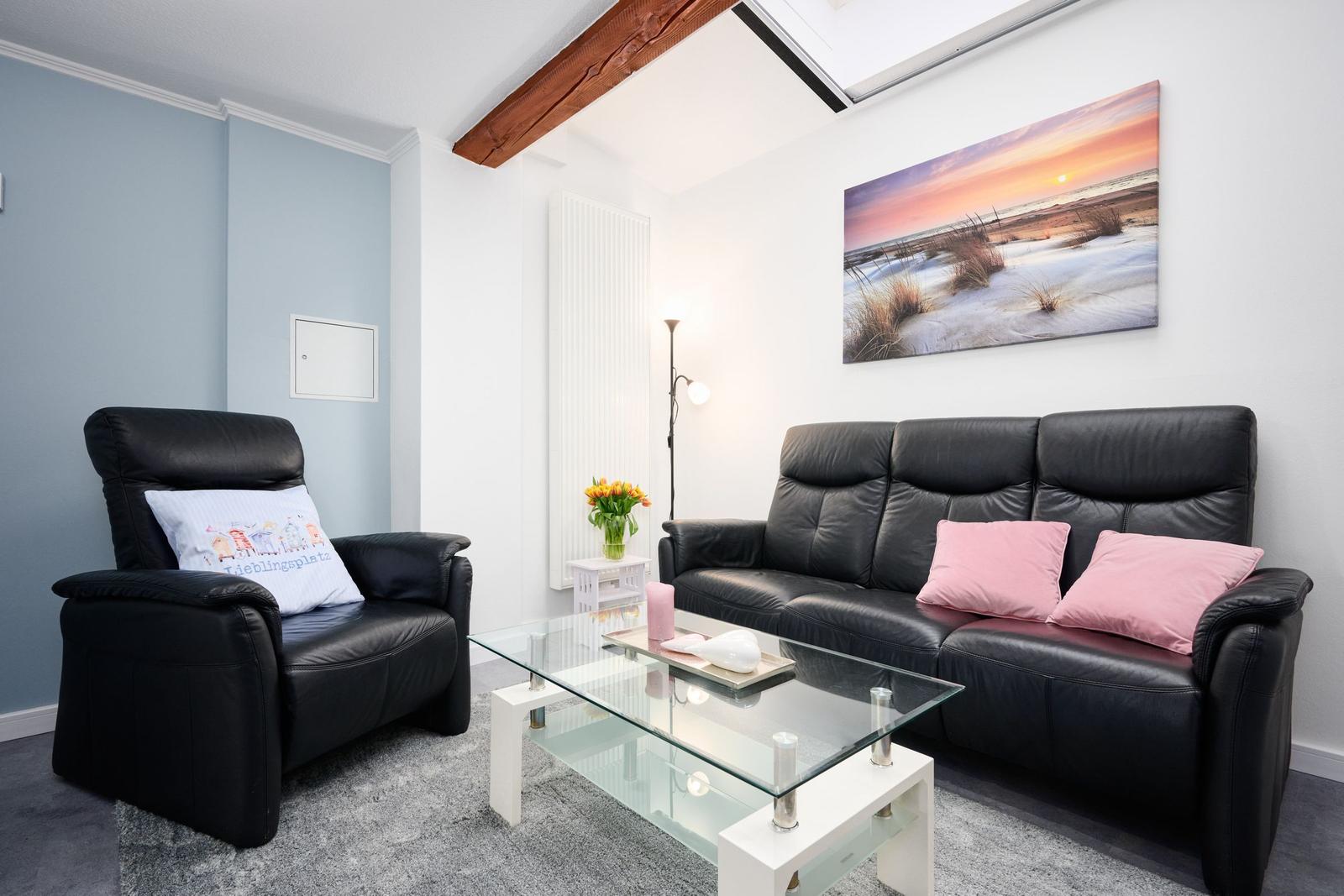 Wohnzimmer mit schwarzer Ledercouch, Glas-Tisch und Wandbild