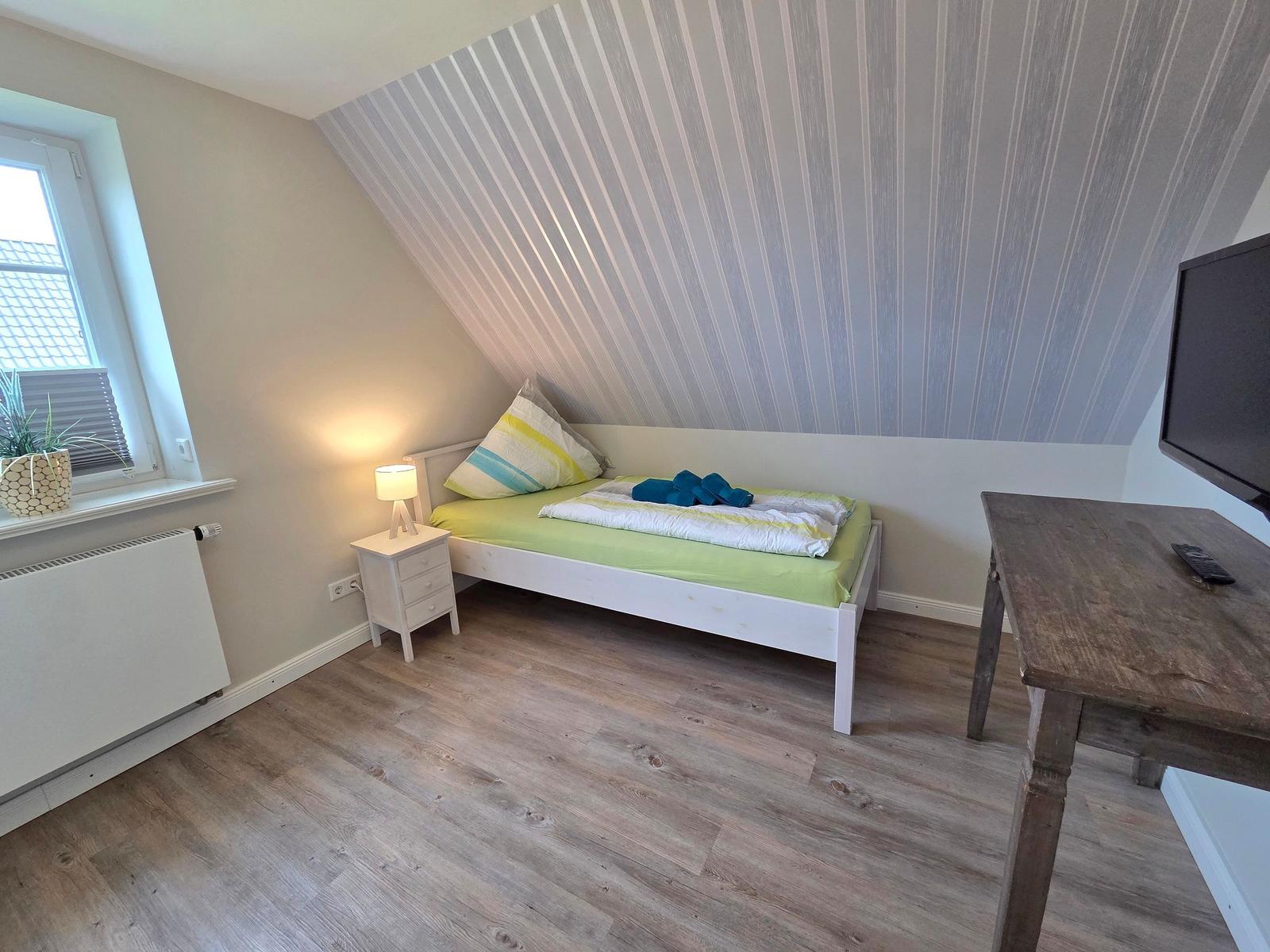 Bedroom with sloped ceiling, bed, nightstand, TV, and wooden table.