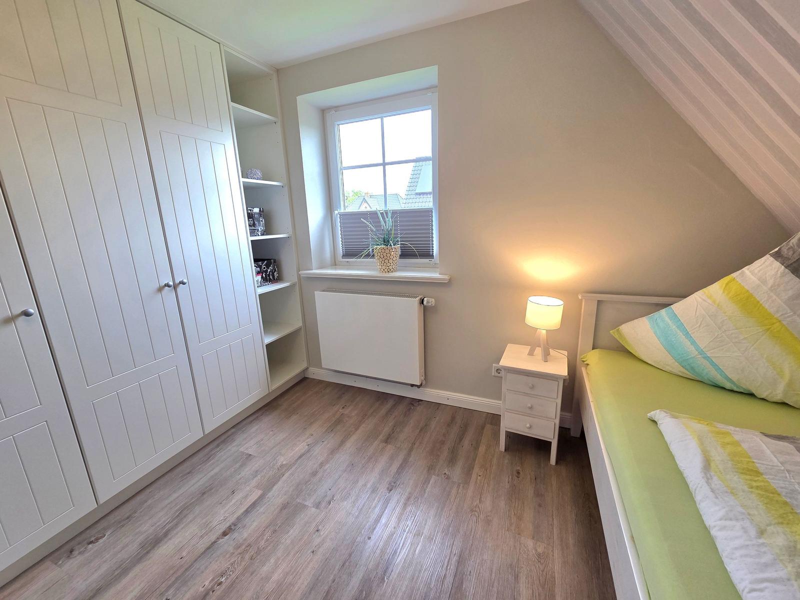 Bedroom with sloped ceiling, white wardrobe, and bed with green sheets.