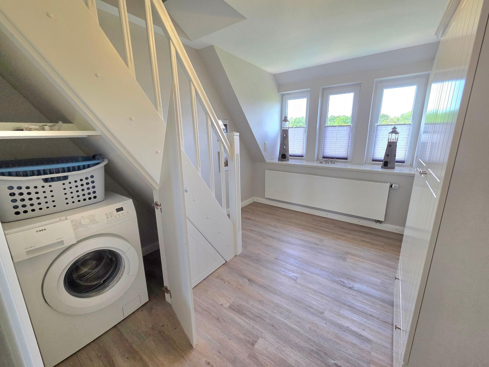 Living space with wooden floor, windows, and washing machine under stairs.