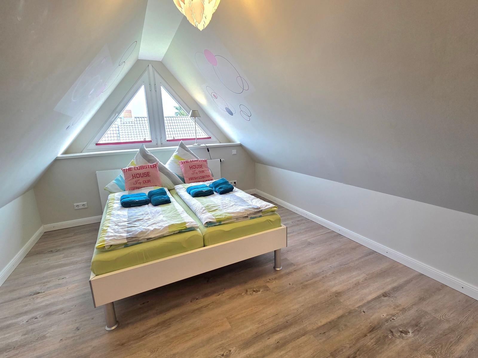 Double bed in attic room with wooden floor and triple window.