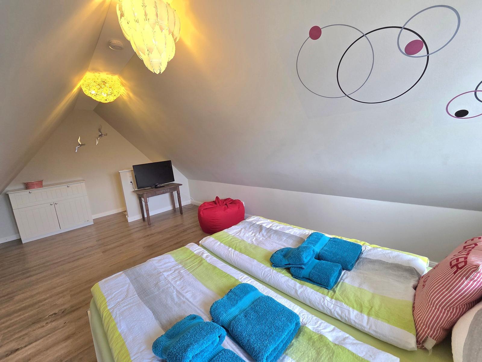 Room with two beds, red bean bag, and wall decoration.