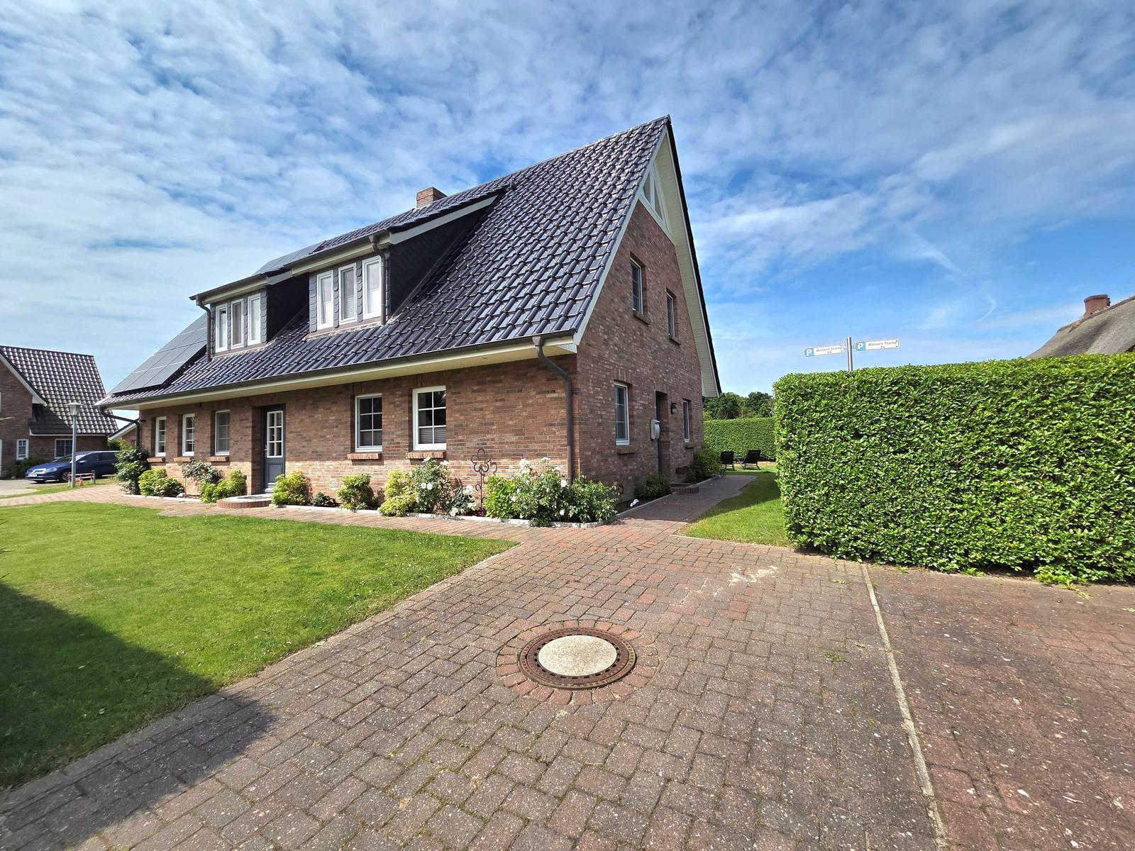 A two-story house with brick facade and dormer windows. Front yard with lawn and plants.