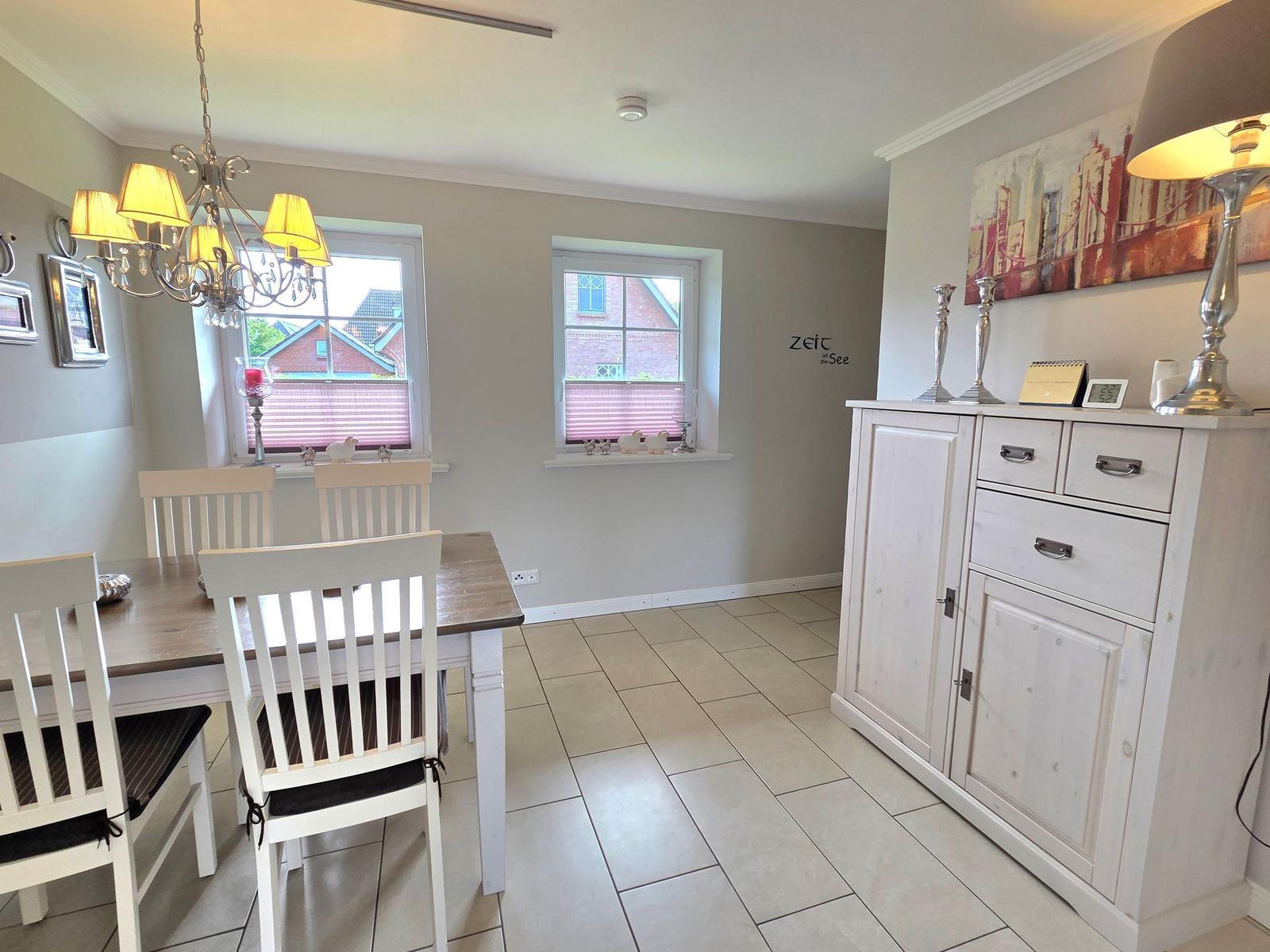 Dining room with table, chairs, windows, and cabinet. Chandelier and wall art.