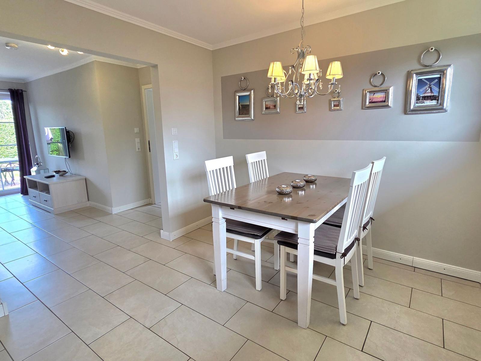 Dining room with table, chairs, and chandelier. Wall decor and TV in background.