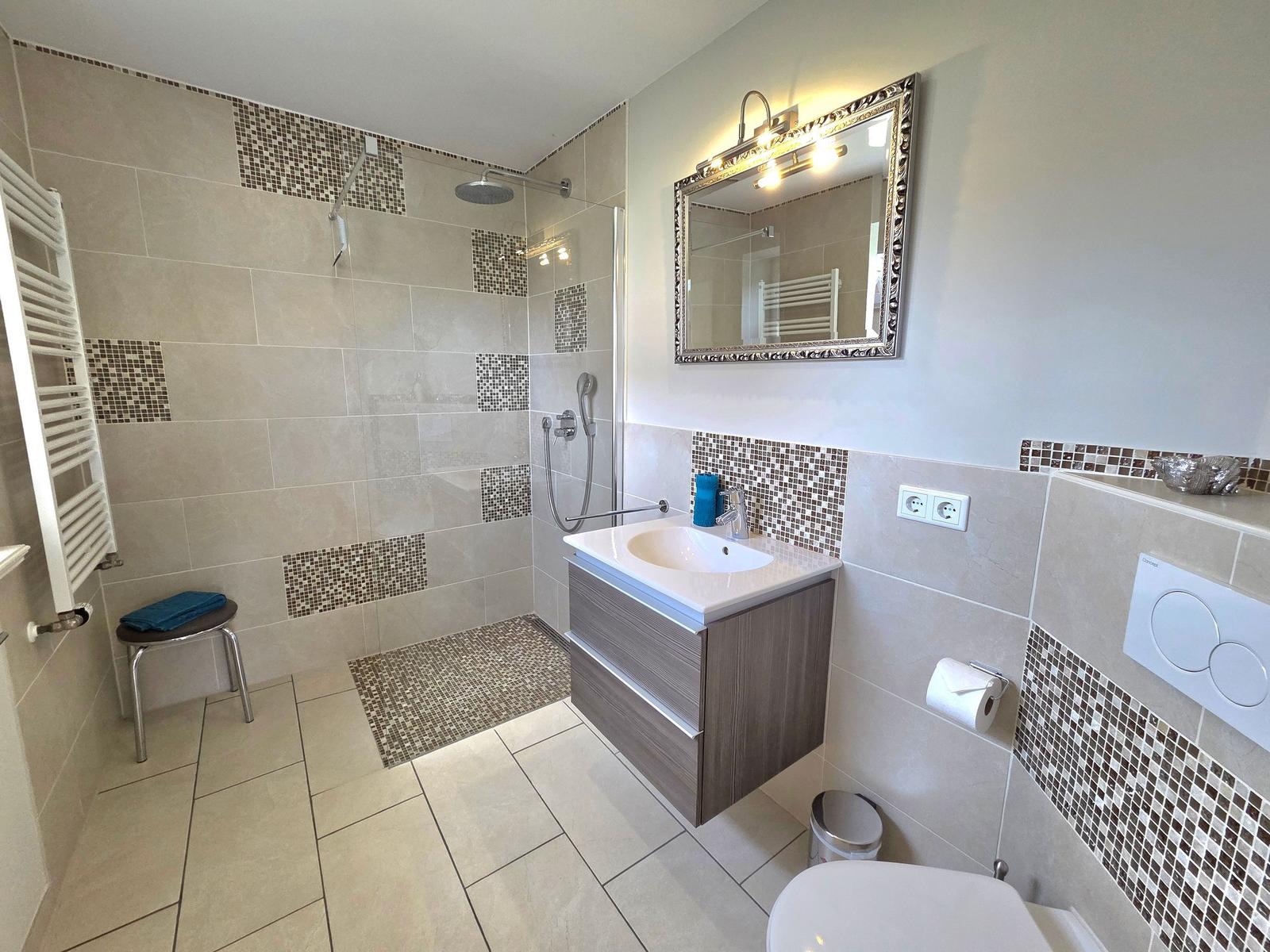 Bath with shower, sink and toilet. Mosaic tiles and mirror.