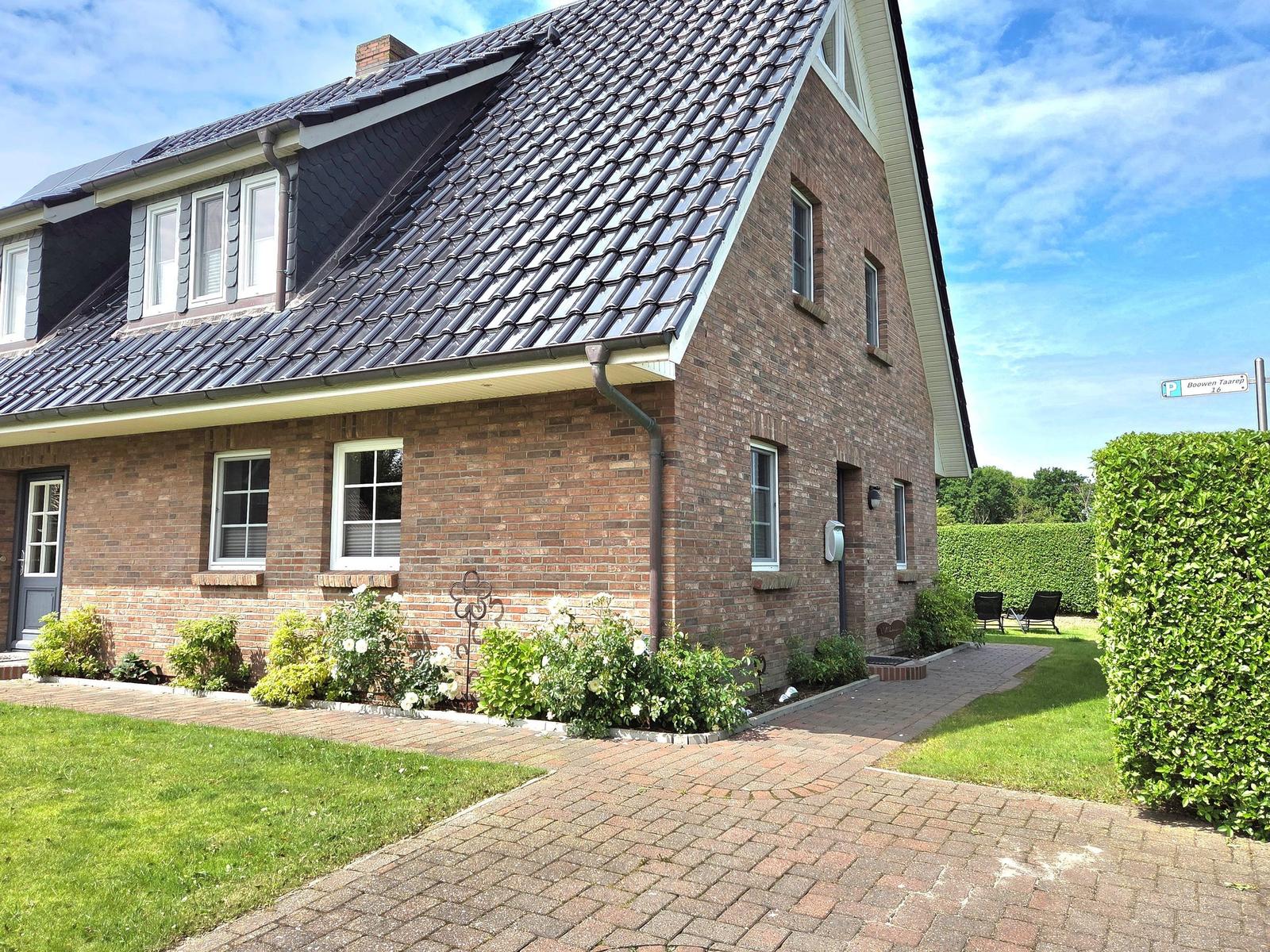 A two-story house with brick facade and dormer windows. Front garden with flower beds and paved path.
