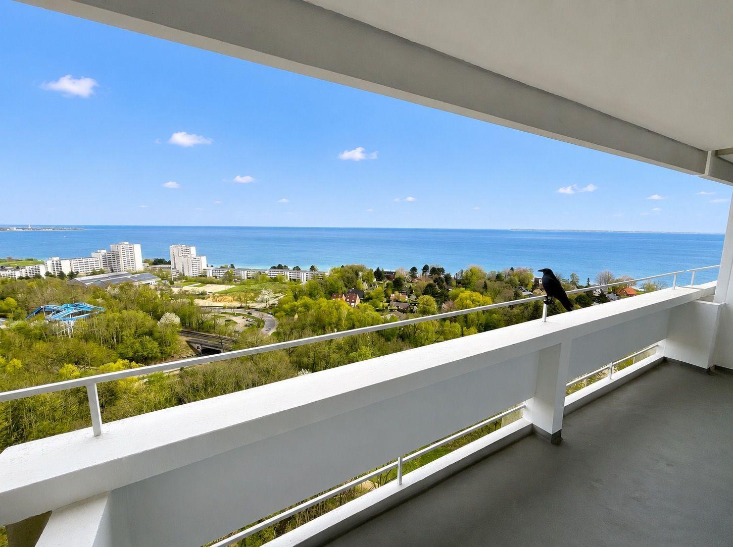 Terrasse mit Blick auf Meer und grüne Landschaft. Ein Vogel sitzt auf der Brüstung.