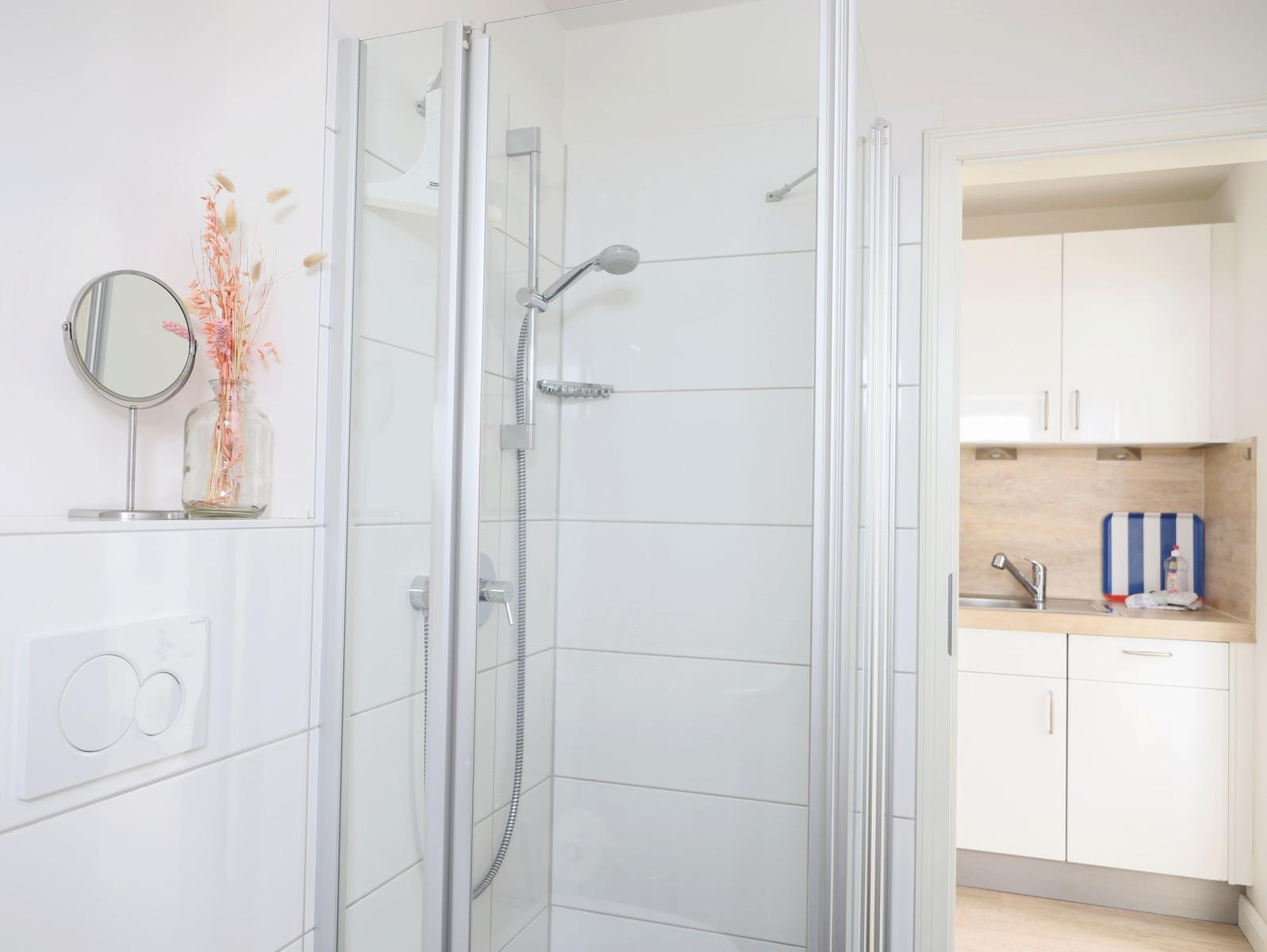 Bad mit Dusche, Spiegel und Vase. Küche mit Arbeitsplatte und Spüle sichtbar.