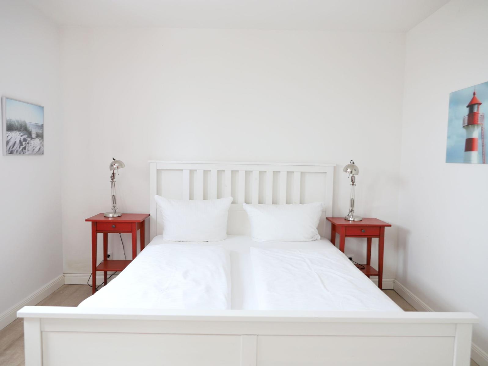 Ein Schlafzimmer mit weißem Bett, zwei roten Nachttischen und Lampen an den Seiten.